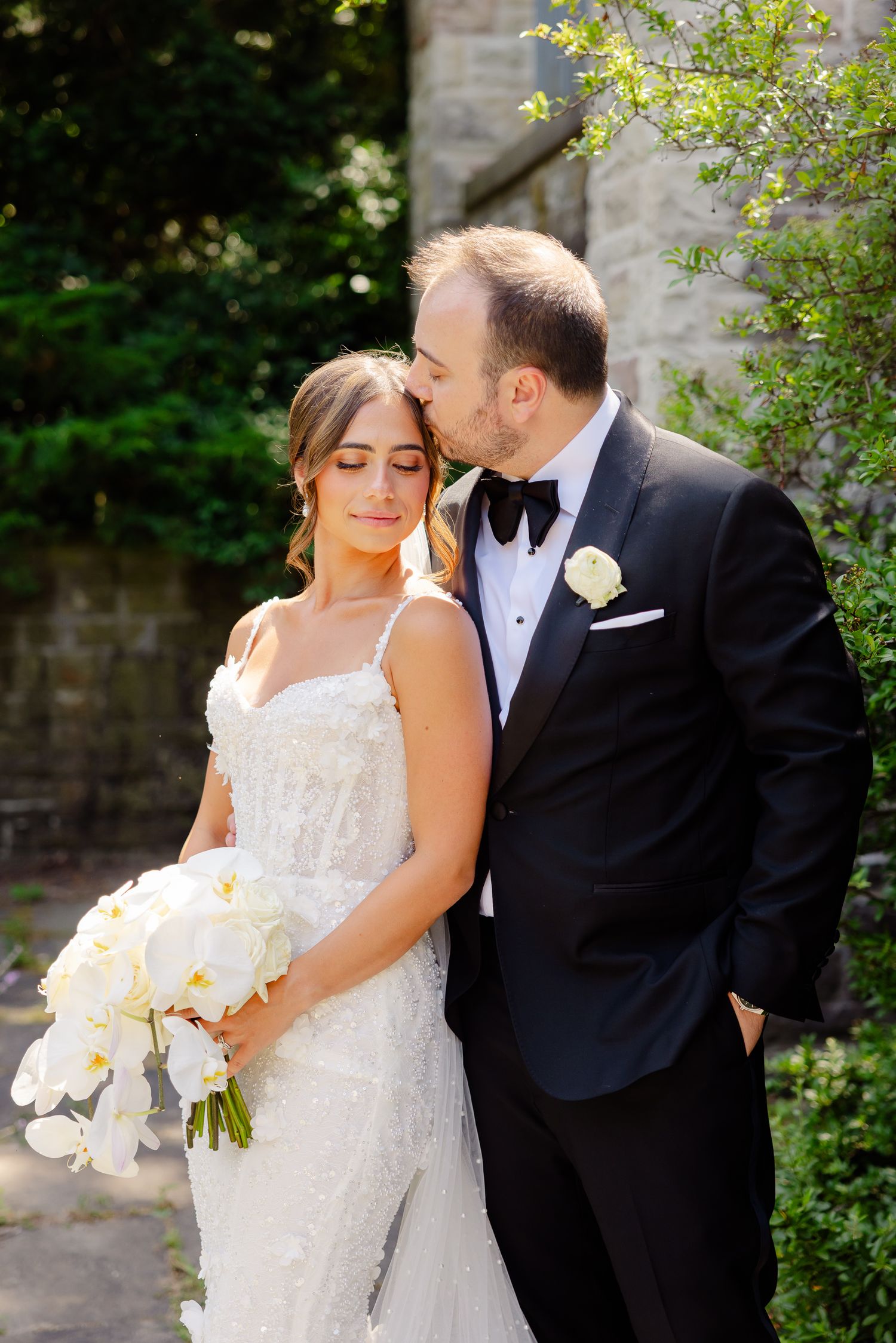A romantic wedding portrait of a couple outdoors, with the bride holding a white orchid bouquet.