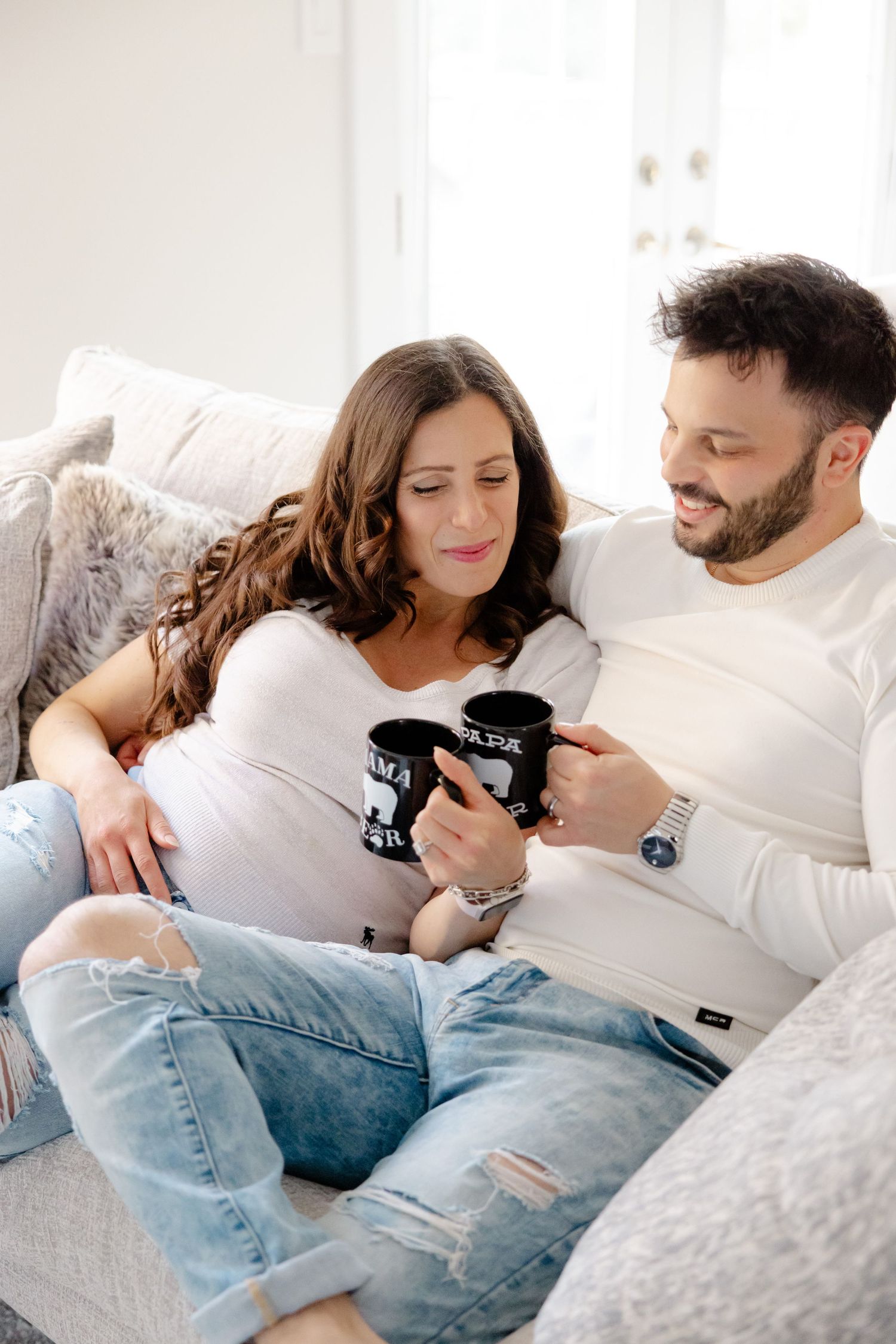 A couple relaxes on a couch, drinking coffee from mugs and enjoying each other's company.
