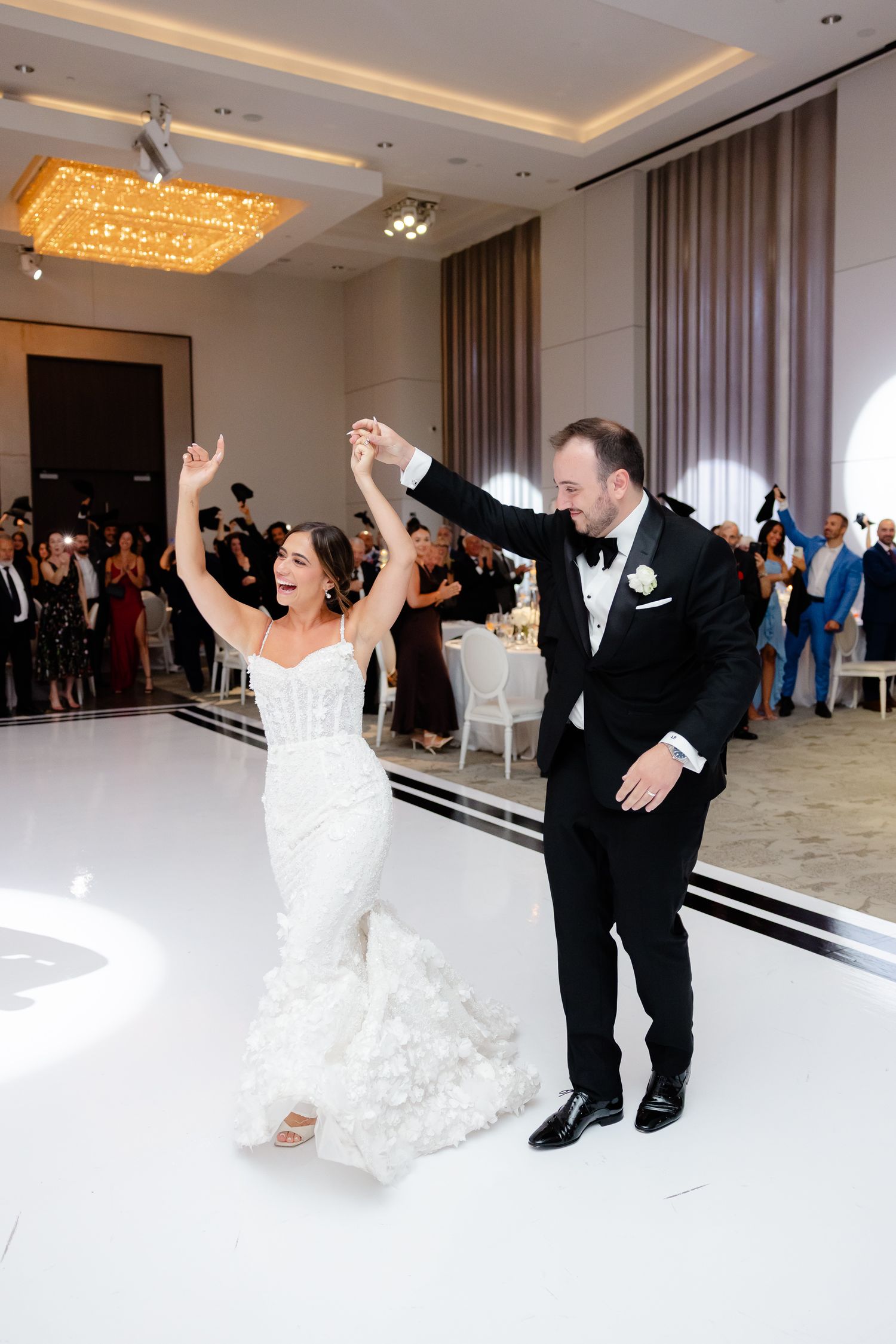 Wedding couple performs choreographed dance sequence in elegant reception hall with crystal chandeliers.