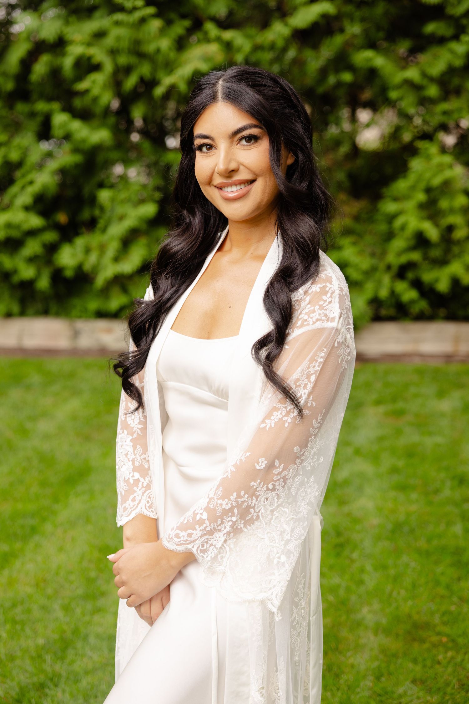 A person wearing a white lace dress poses for an outdoor photo session in a lush green garden setting.