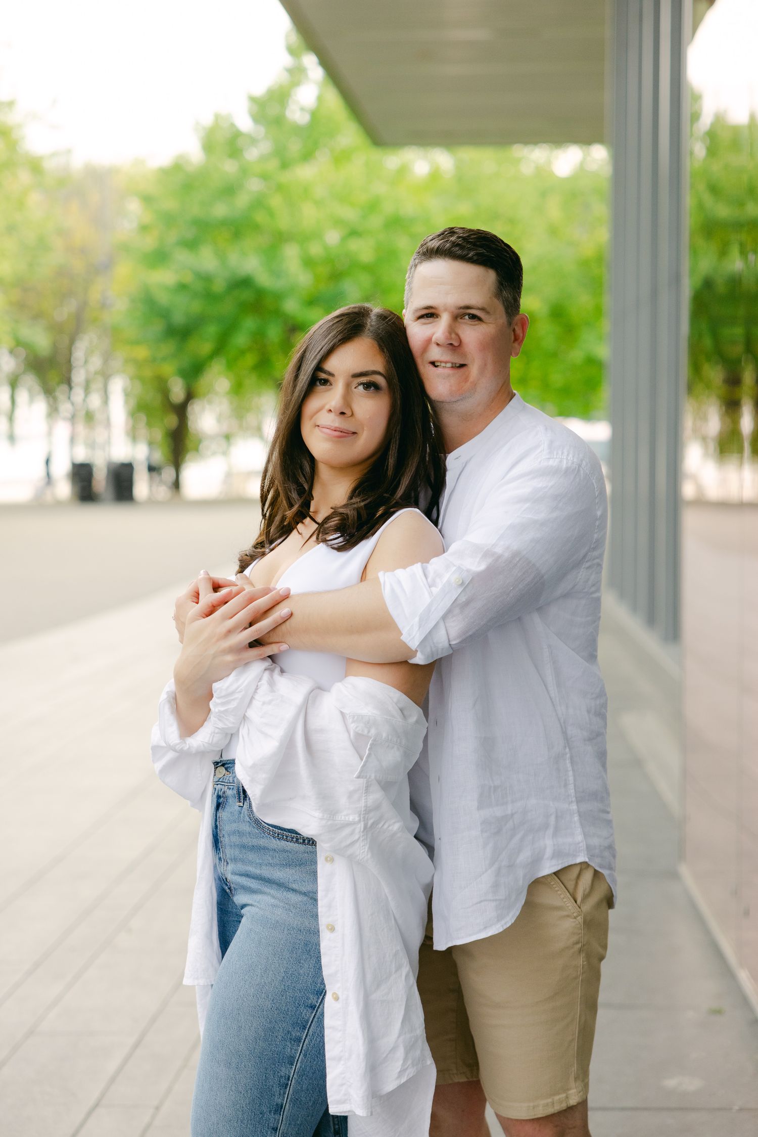 A romantic couple poses together against architectural columns and glass windows.