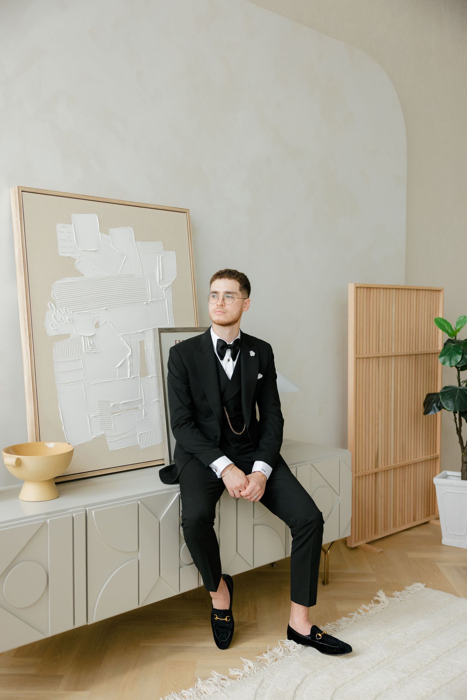 Sophisticated black tuxedo with loafers and vest showcased in a minimal modern interior setting.