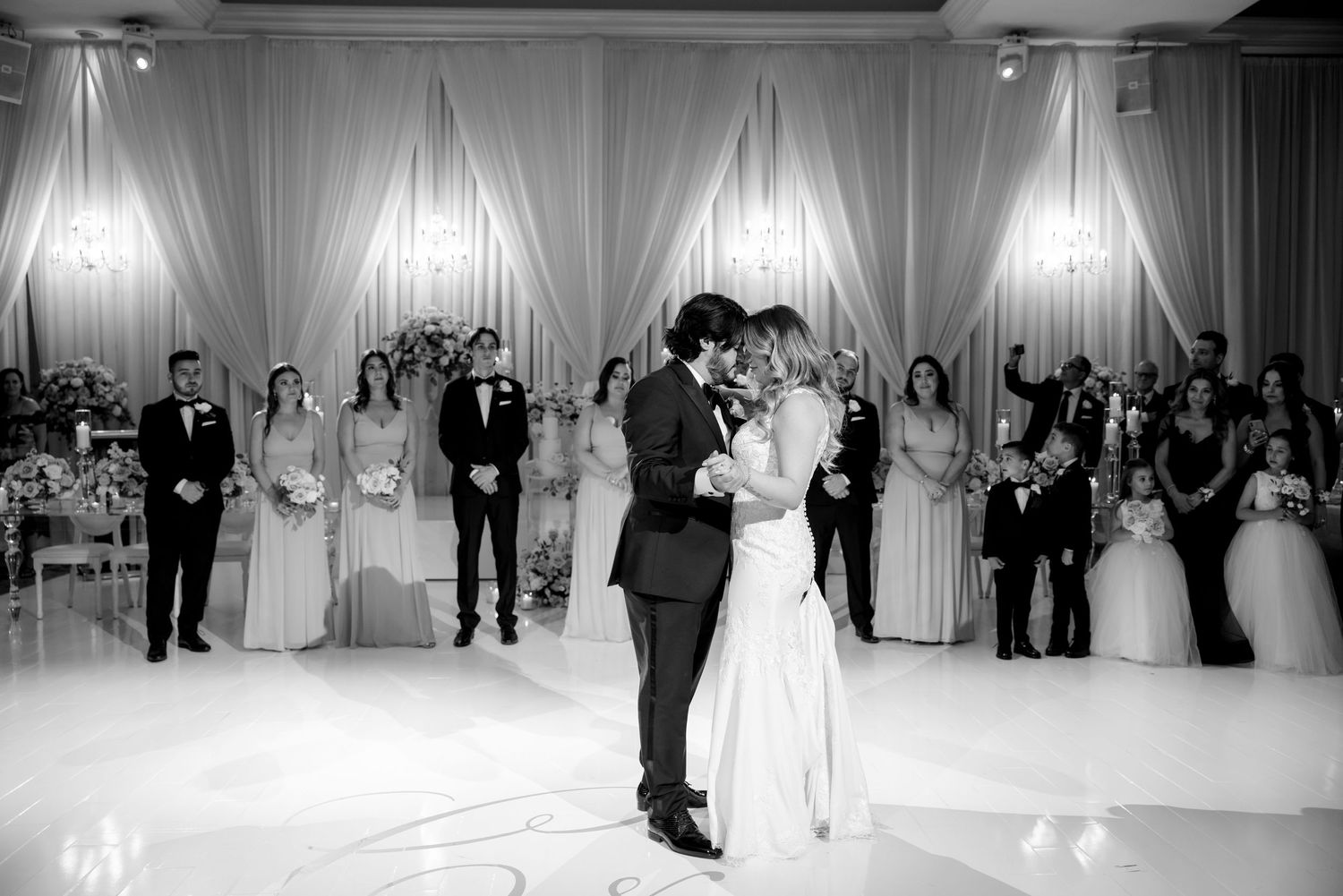 Black and white photo of couple's first dance with bridal party watching.