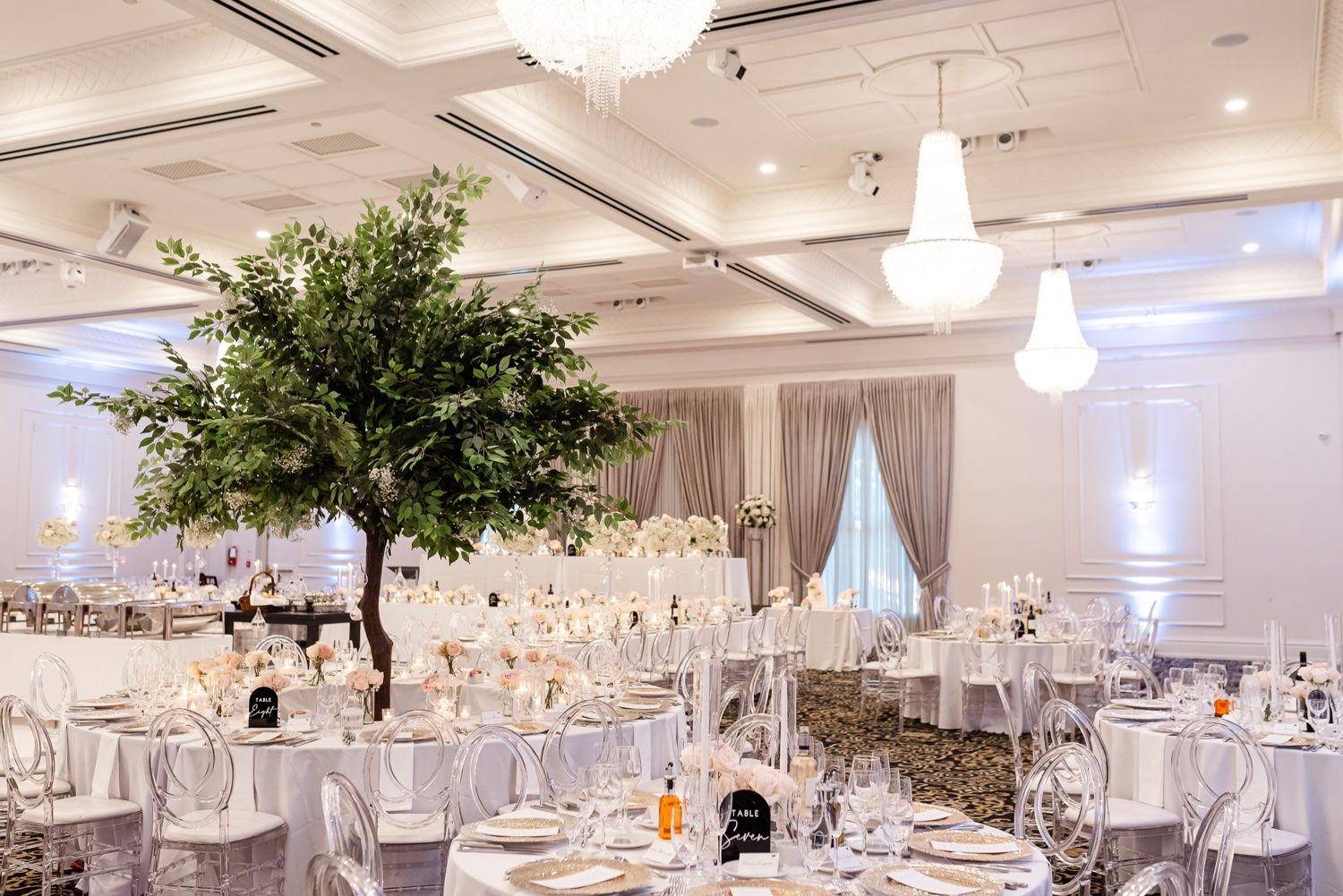 Elegant wedding reception ballroom with large decorative trees and white table settings.