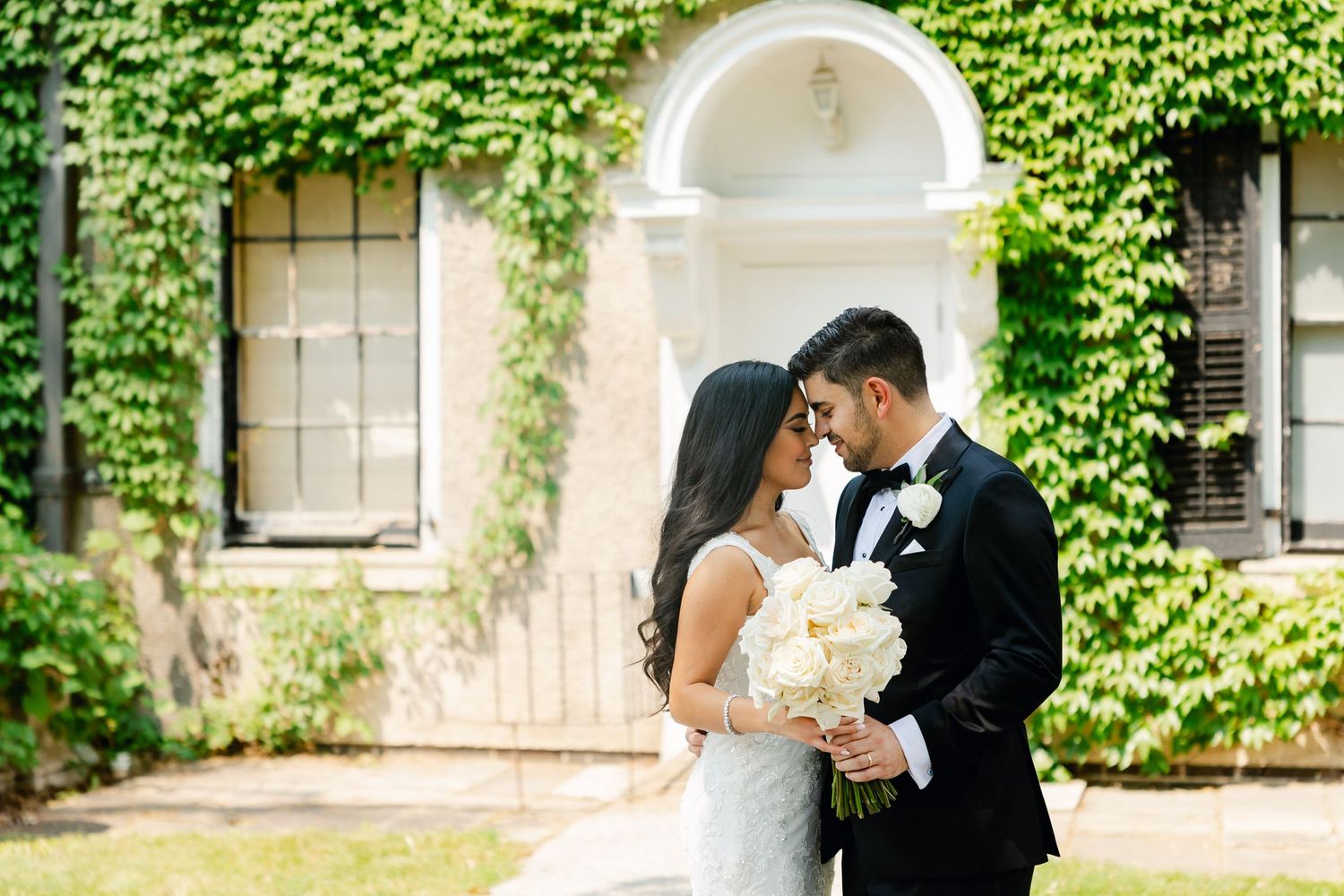 Elegant wedding portrait against a backdrop of ivy-covered walls and white architectural details.