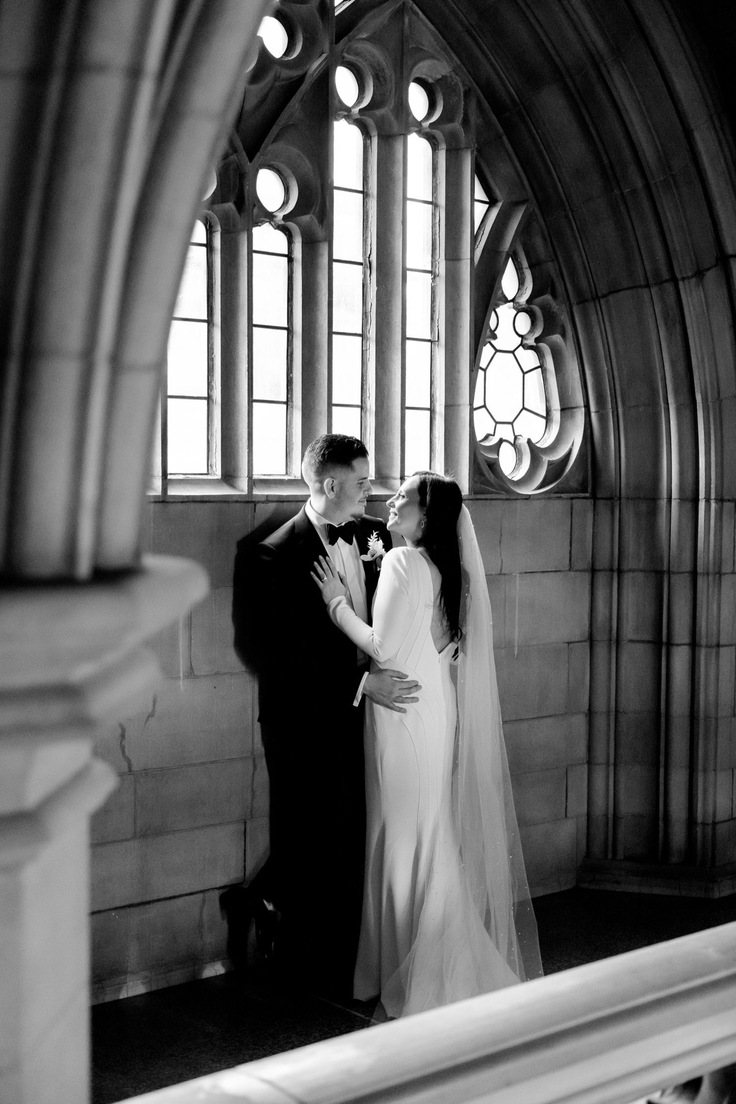 Black and white wedding portrait framed by gothic windows and dramatic stone arches.