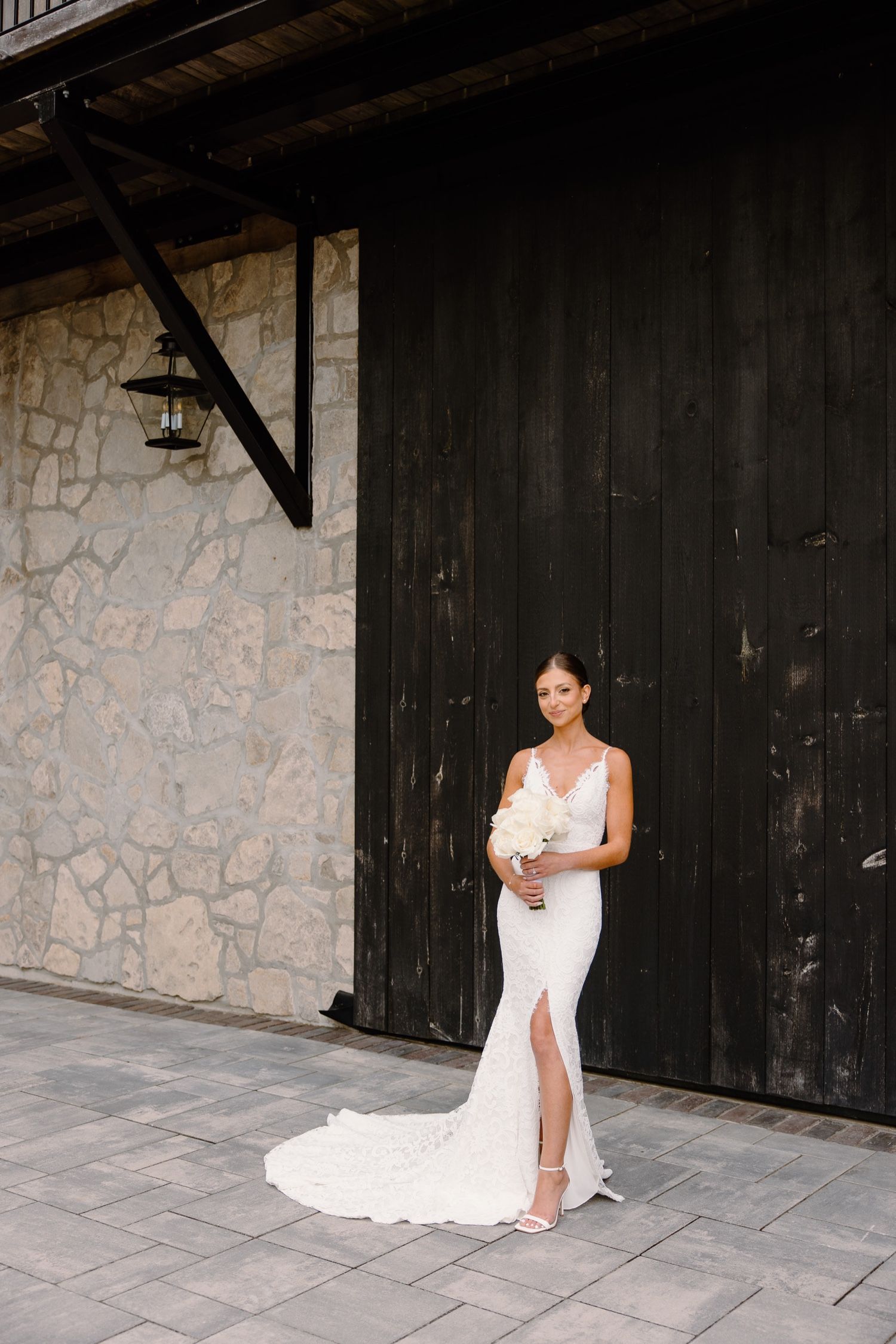 Full length bridal portrait against rustic stone and wood backdrop.