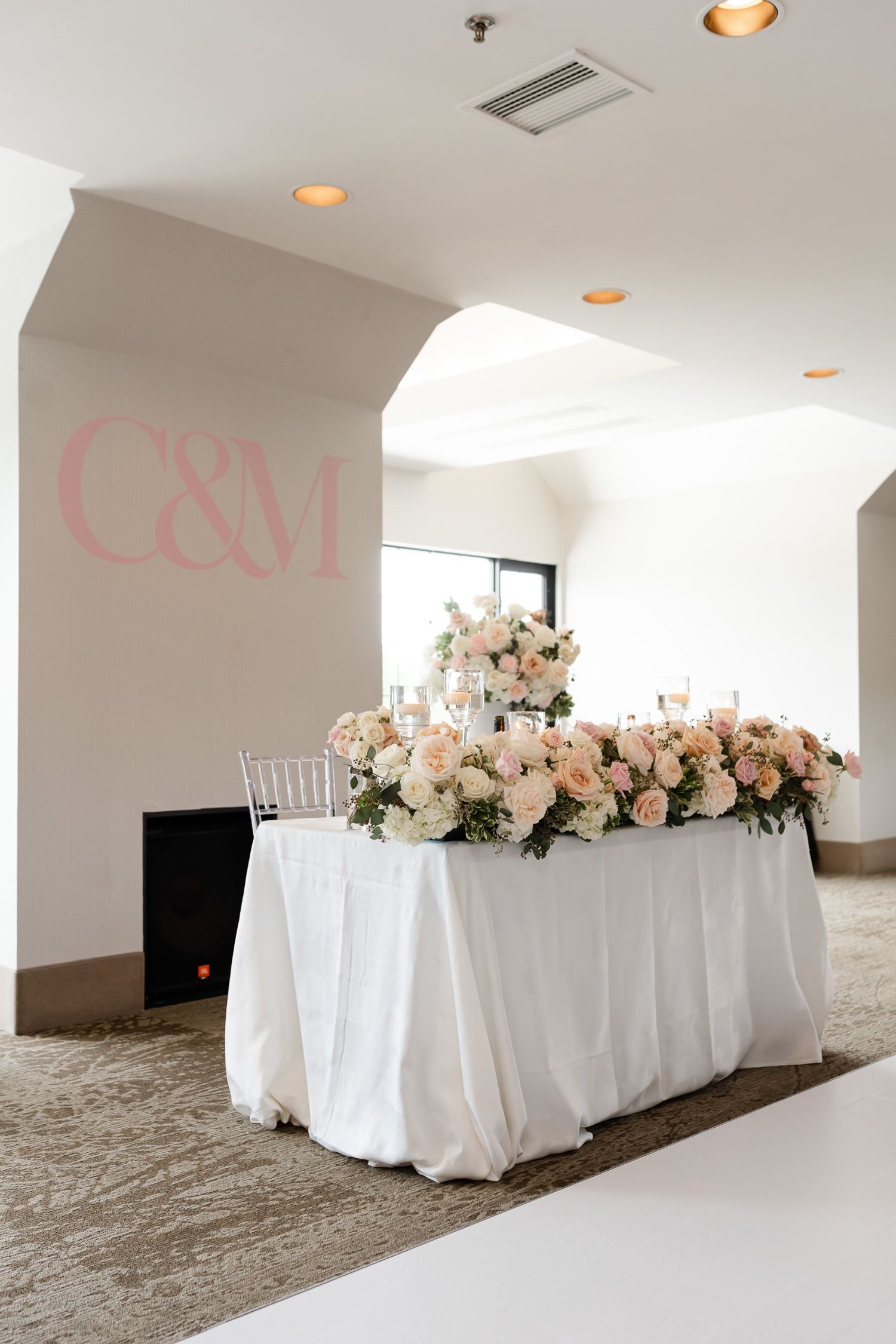 Wedding reception table with blush pink floral arrangements and white linens.