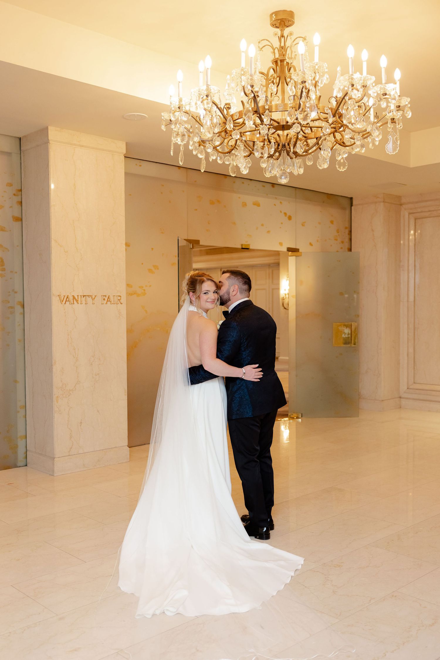Elegant wedding couple sharing intimate moments in a luxurious white ballroom with crystal chandeliers.