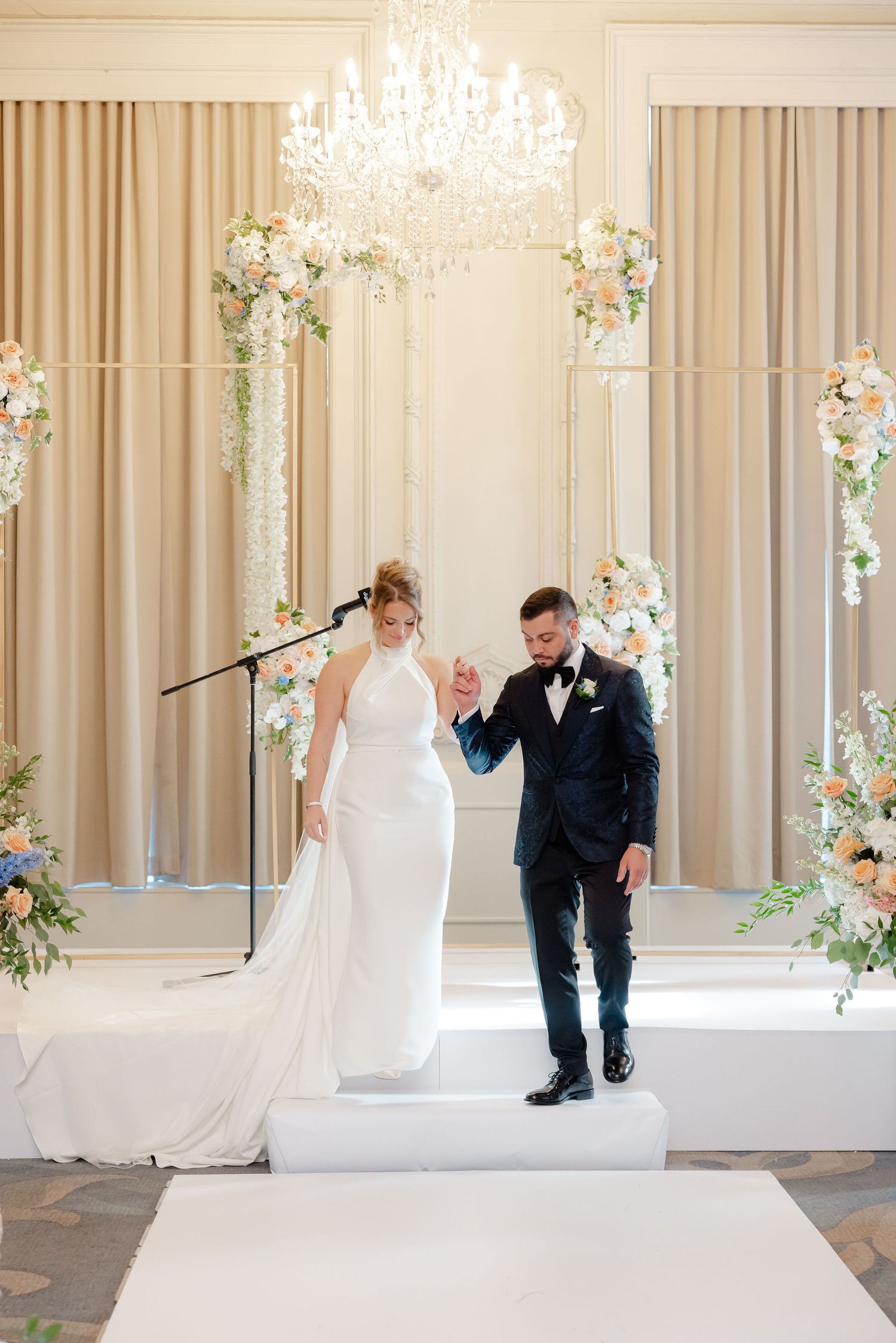 Elegant wedding ceremony setup in a bright room with floral arrangements and flowing beige curtains.