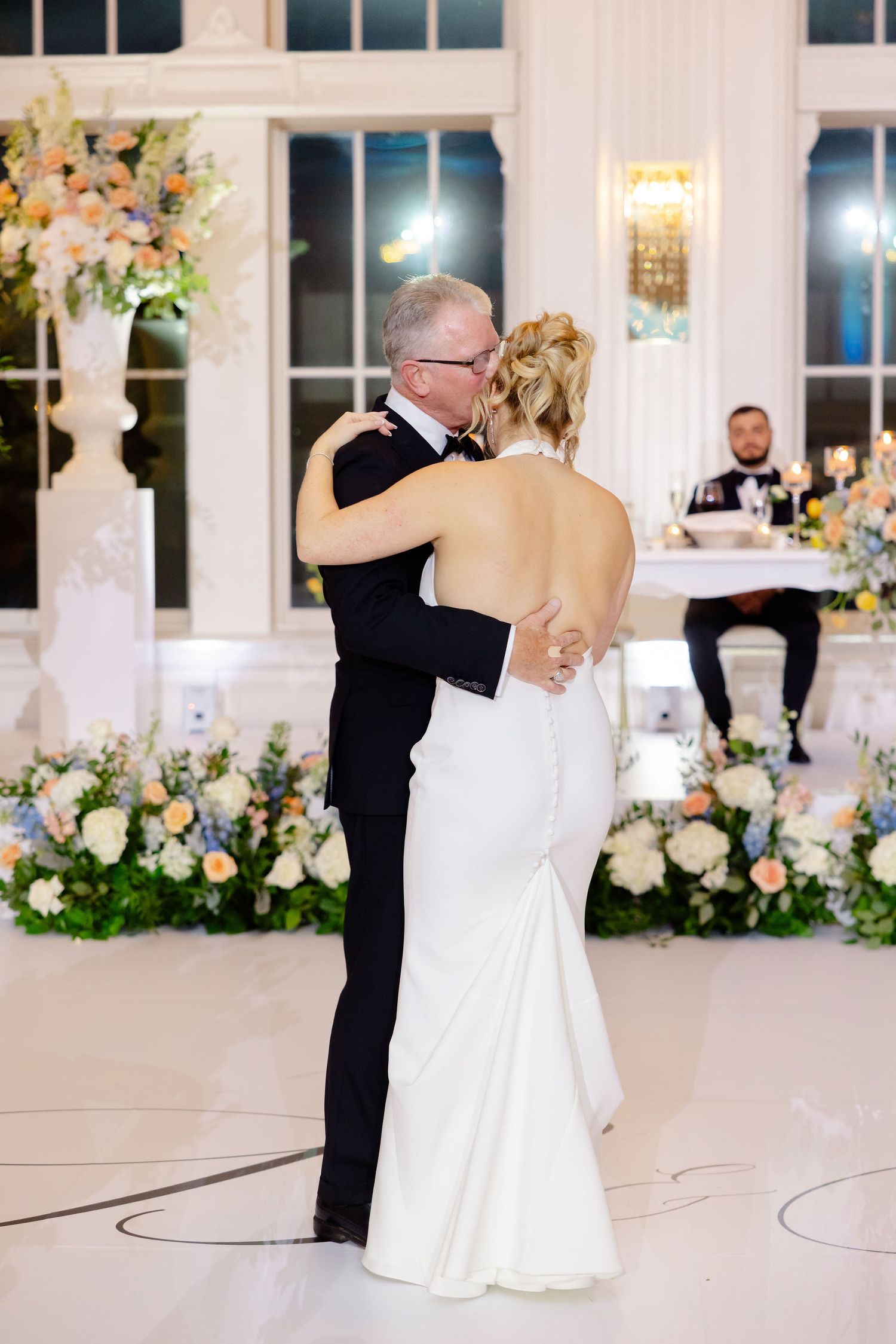 A tender dance moment captured during a wedding reception in an elegant white-walled ballroom.