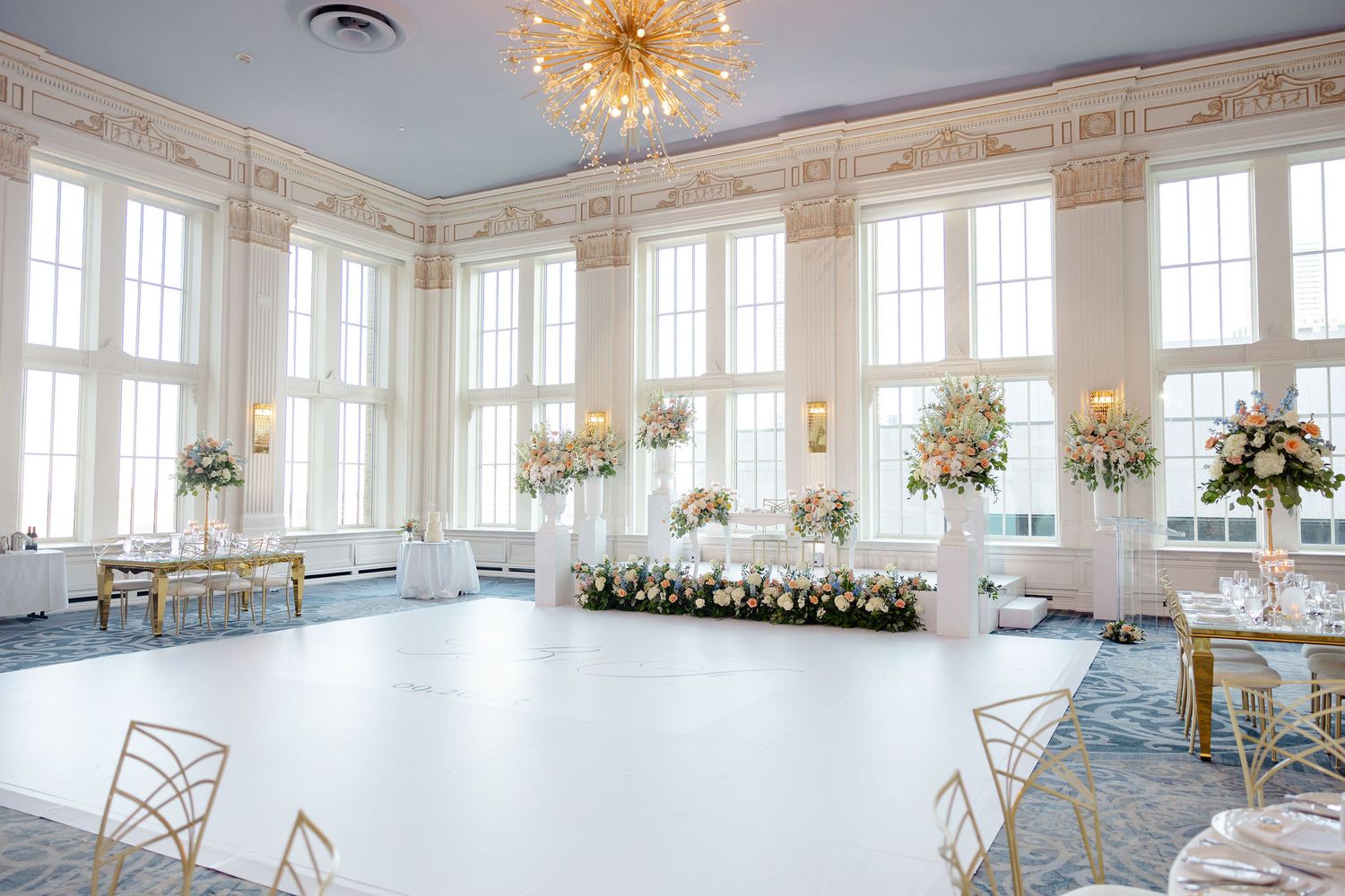 Panoramic view of a luxurious white ballroom with crystal chandelier and large windows.