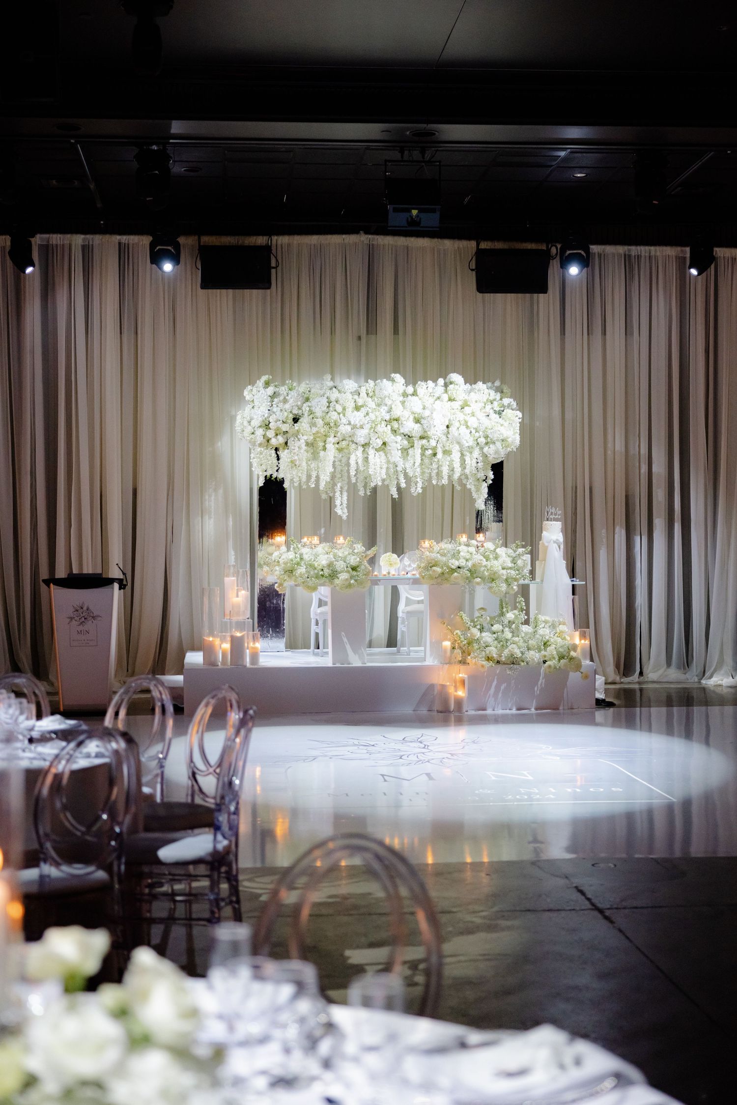 Elegant ballroom setup with dramatic lighting and flowing fabric backdrop for wedding reception.