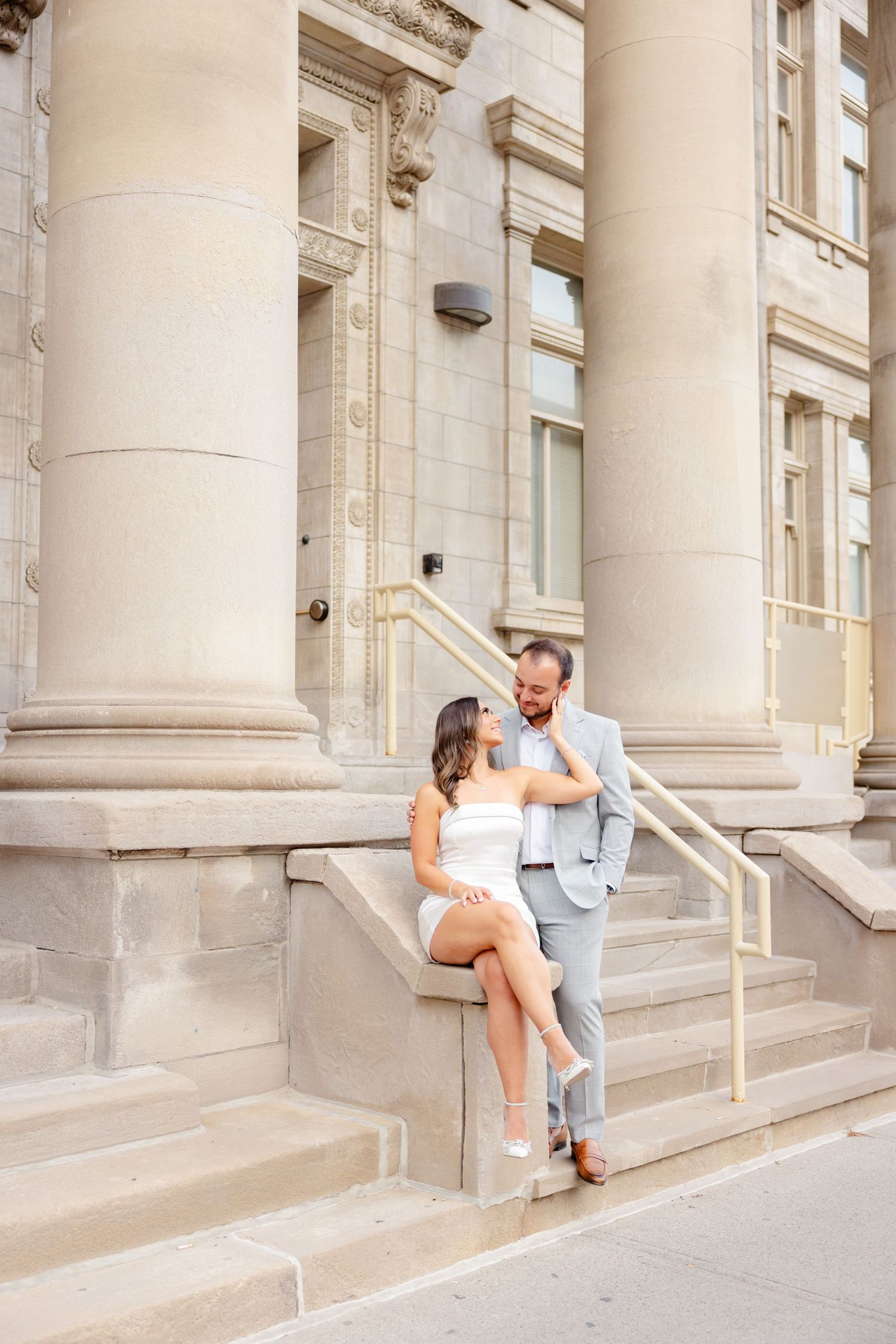 Couple shares intimate moment on grand stone steps of historic building with columns.