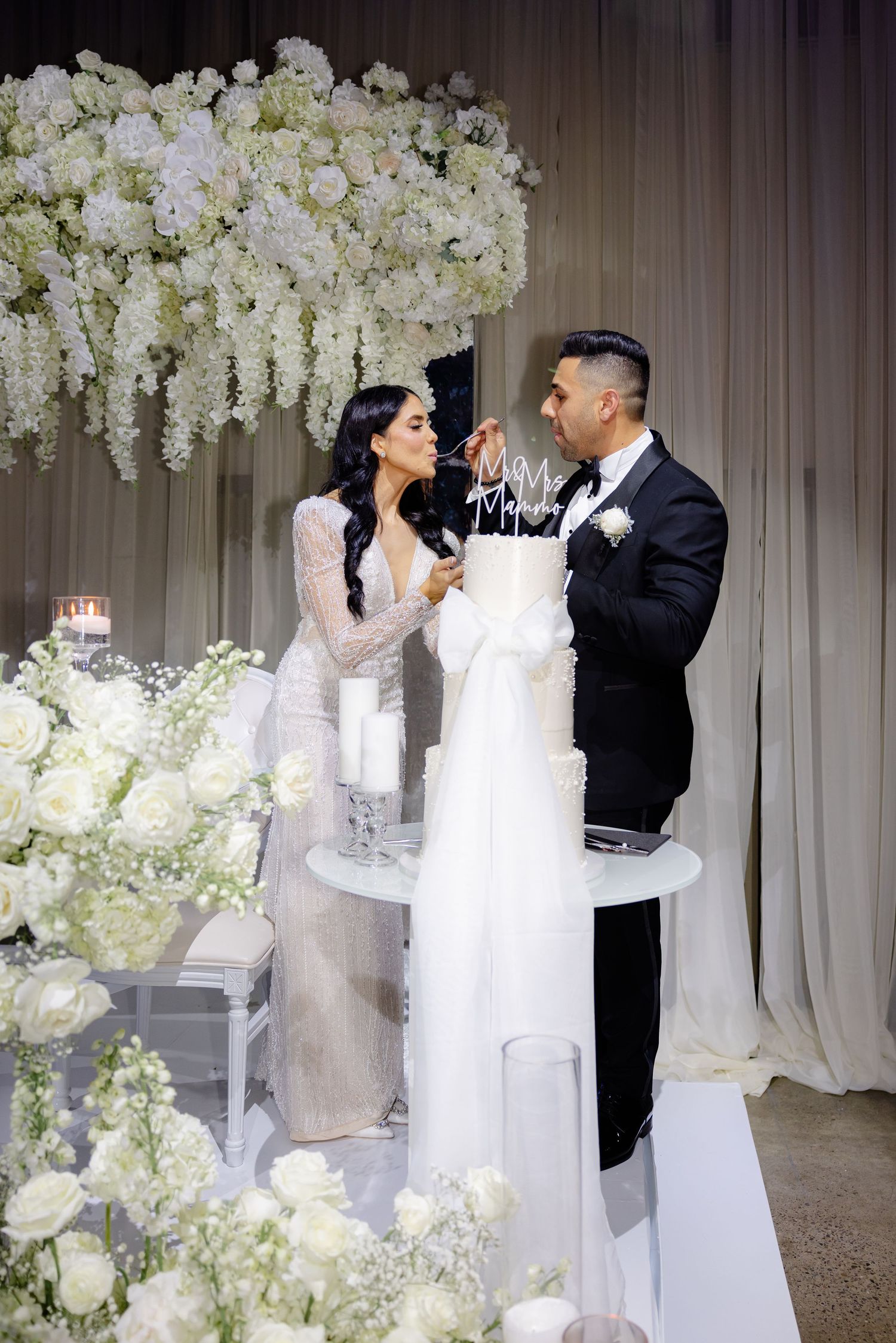 Couple shares a fun cake-feeding moment at their flower-filled wedding reception.