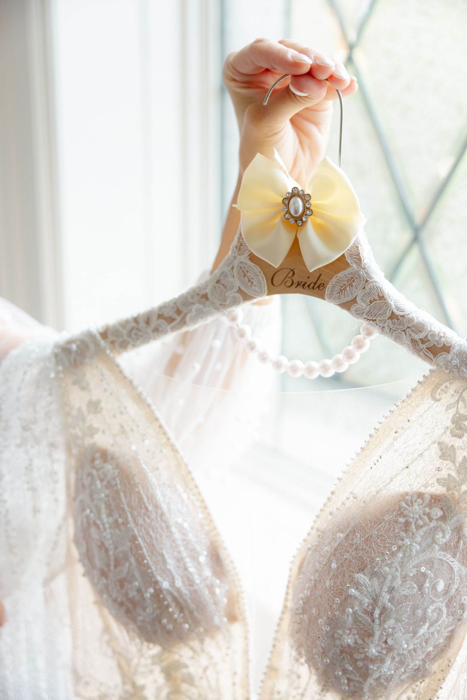 Close-up of an elegant white lace wedding dress on a decorative hanger with yellow bow detail.