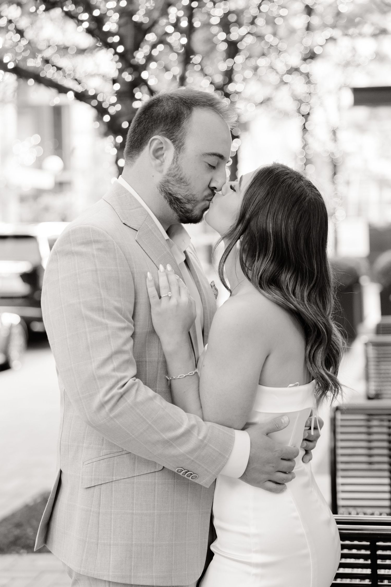 Black and white portrait of couple sharing tender moment under lit trees.