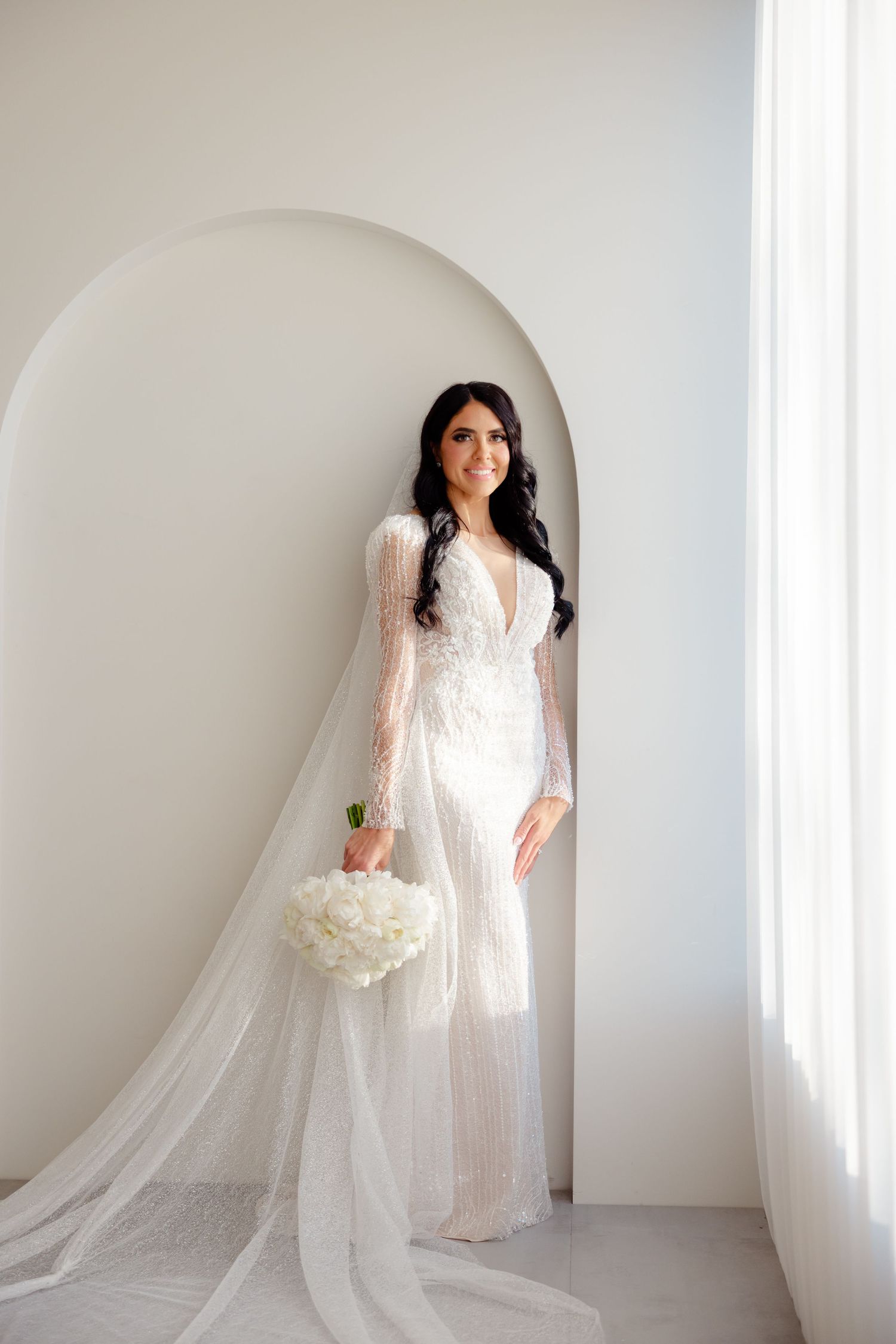 Ethereal bridal portrait with long veil in modern white architectural setting.