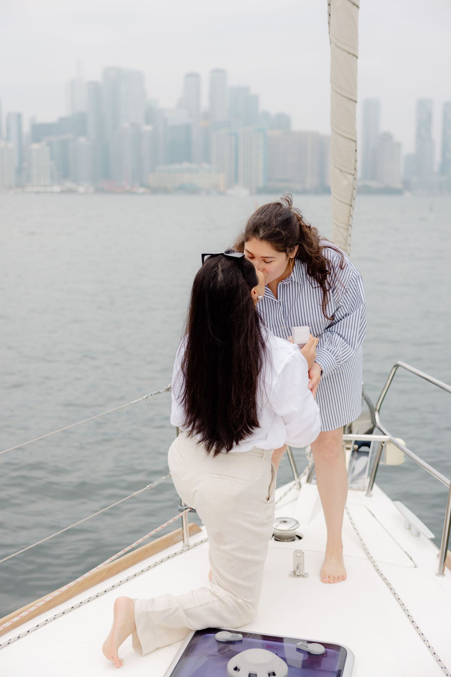 Two people share an intimate moment on a boat with the Manhattan skyline visible in the misty background.