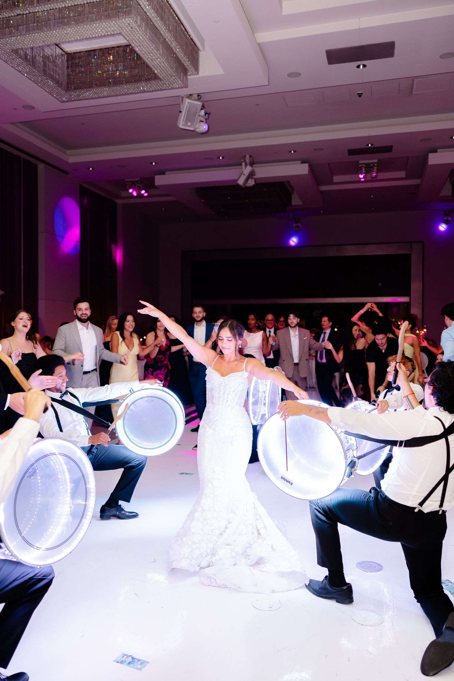 Wedding guests create a light painting effect with LED tubes during a reception in a banquet hall with purple lighting.
