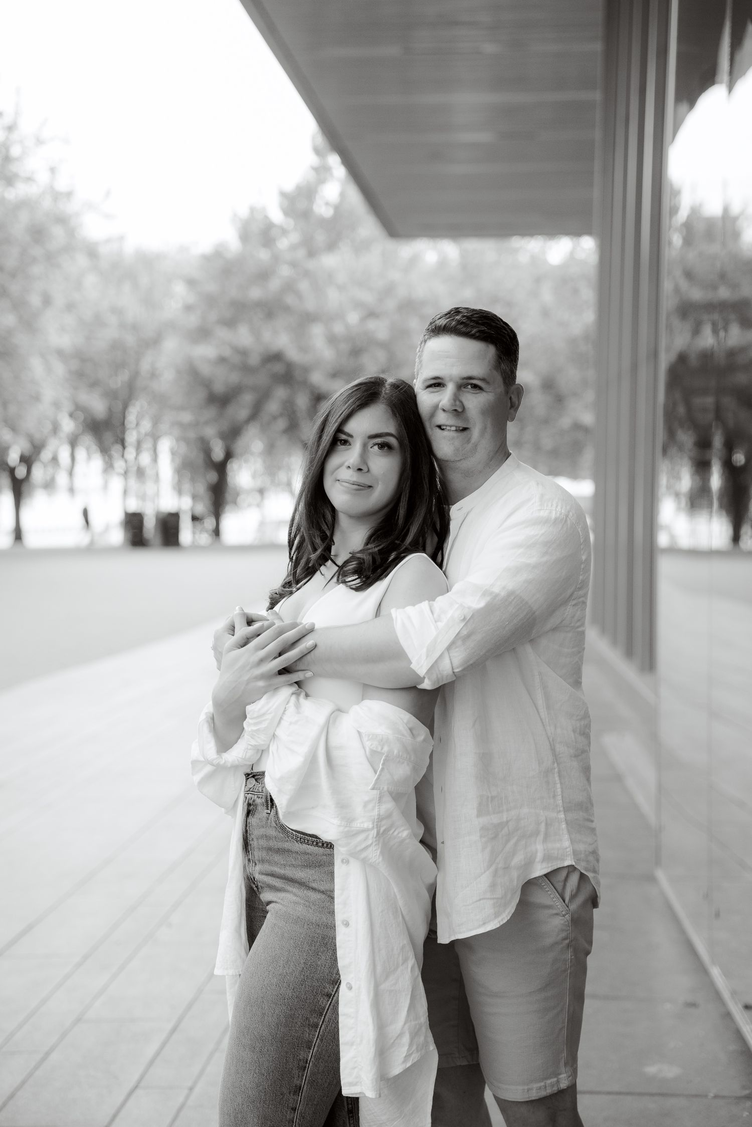 Black and white portrait of a couple embracing in a modern architectural setting.