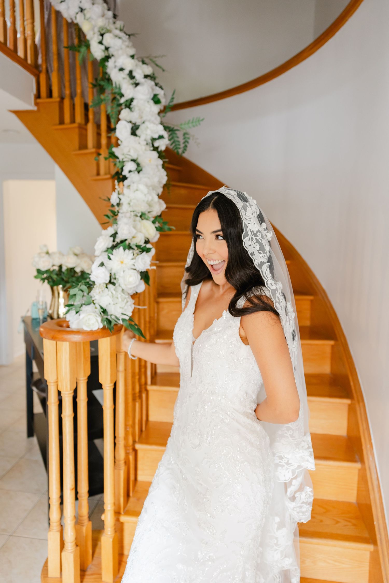 Bride stands on wooden staircase adorned with white flower garland.