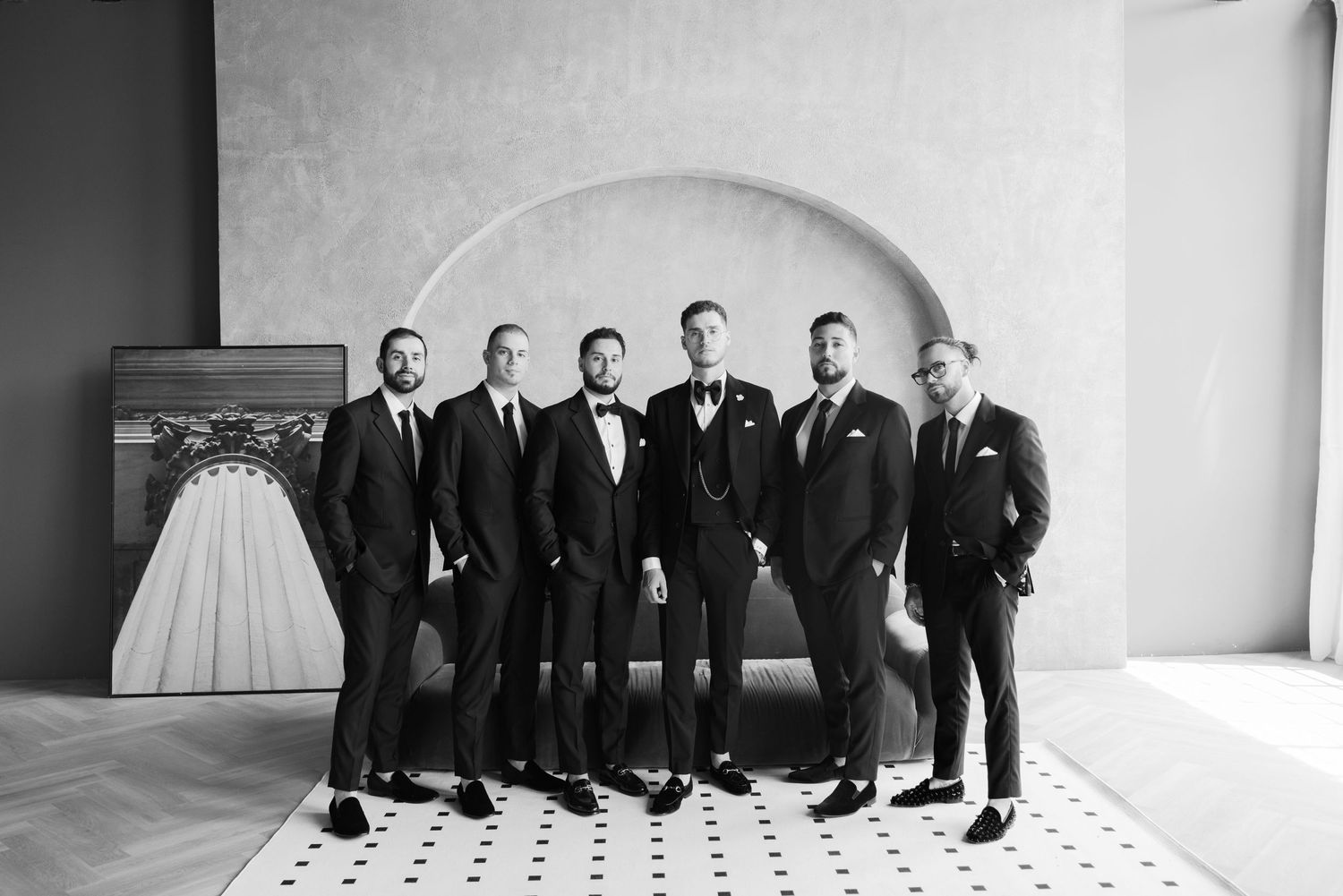 Black and white photo of groomsmen in formal attire standing against a minimalist backdrop.
