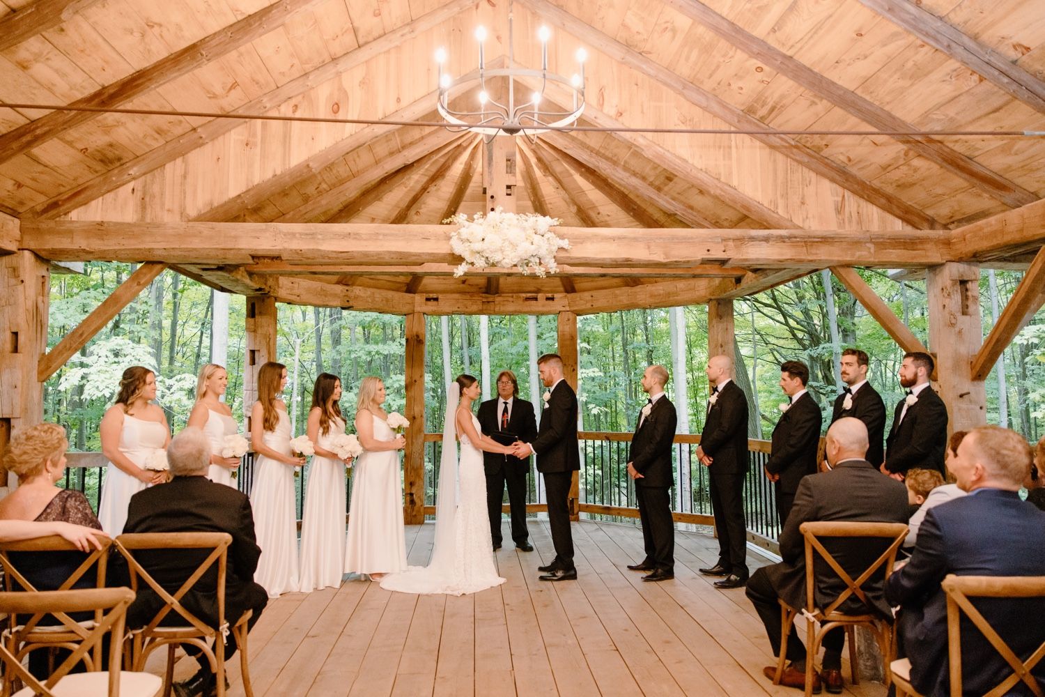 Outdoor wedding ceremony in rustic wooden pavilion surrounded by forest greenery.