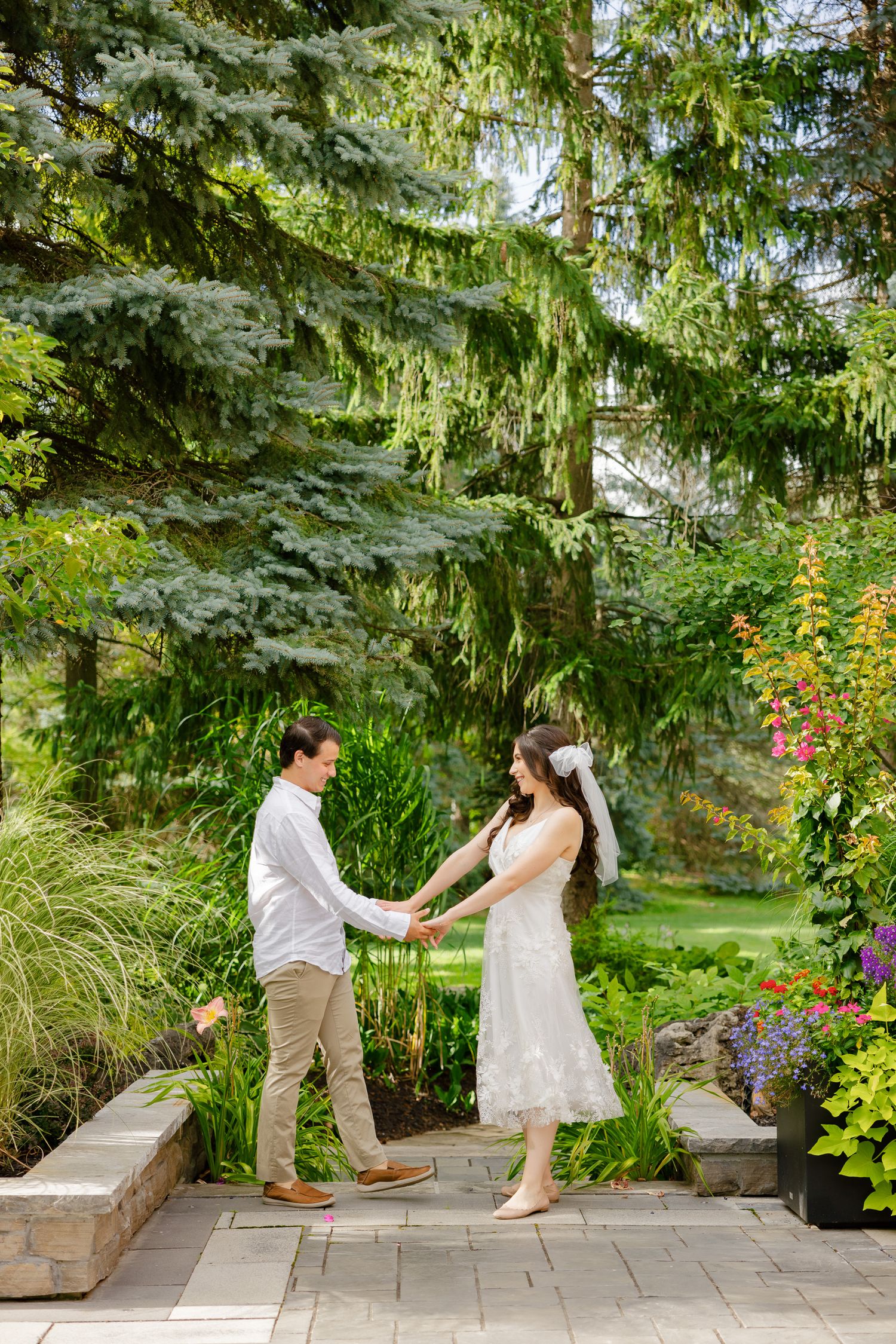 A playful moment between newlyweds as they dance on a stone path surrounded by colorful garden flowers.