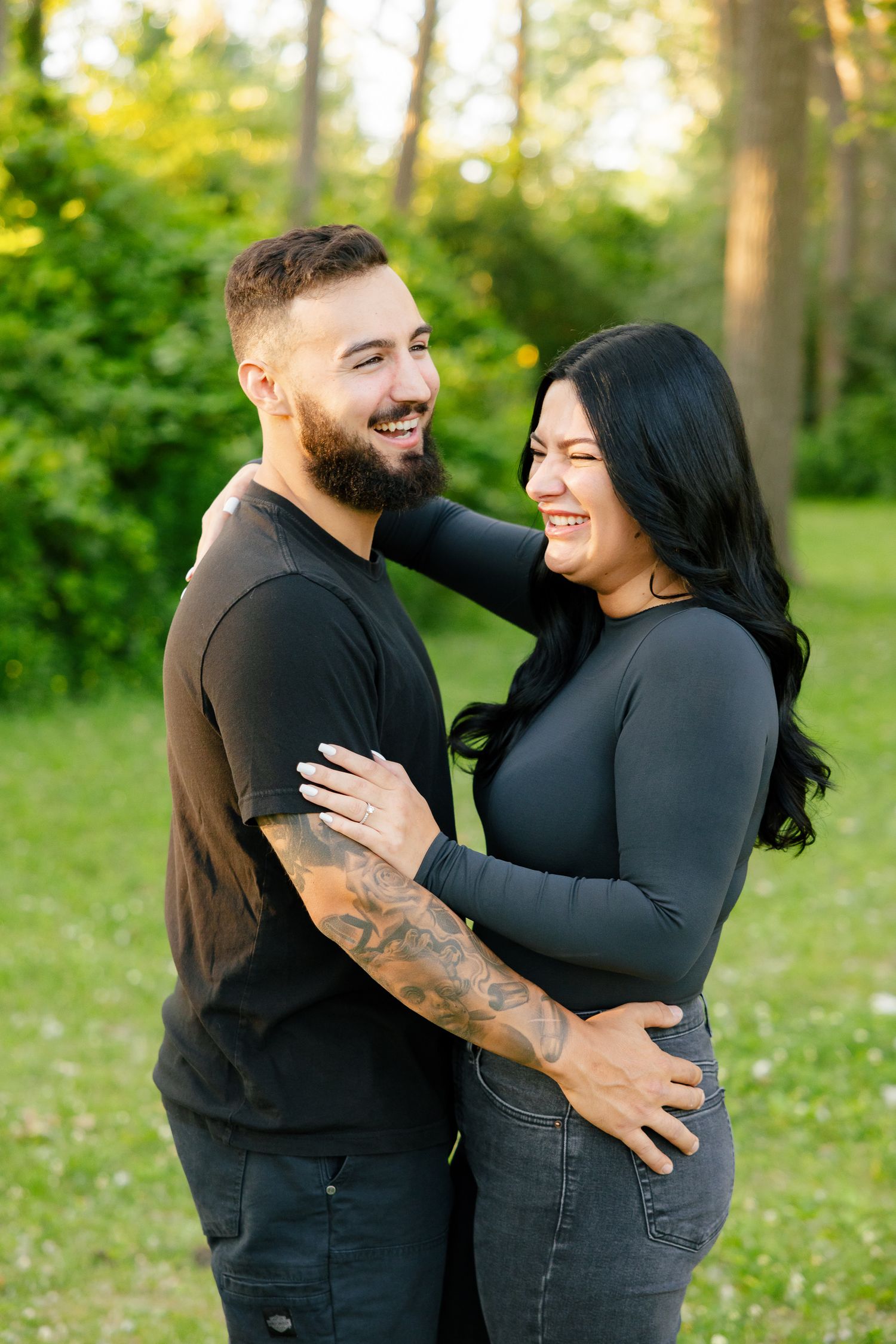 A joyful couple laughs together while embracing in a sunny forest clearing.