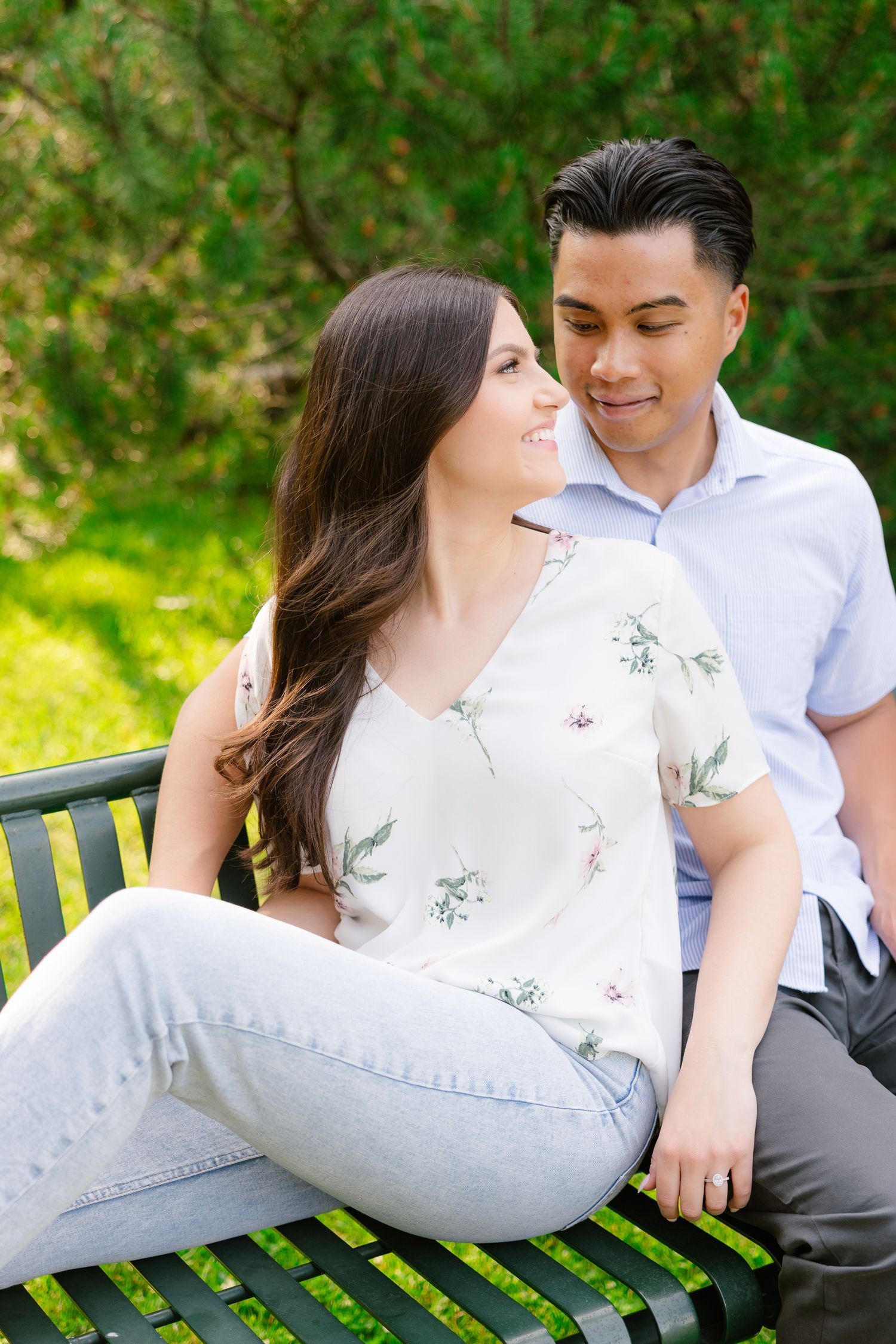 A couple shares a tender moment while sitting together on a green park bench in a garden setting.
