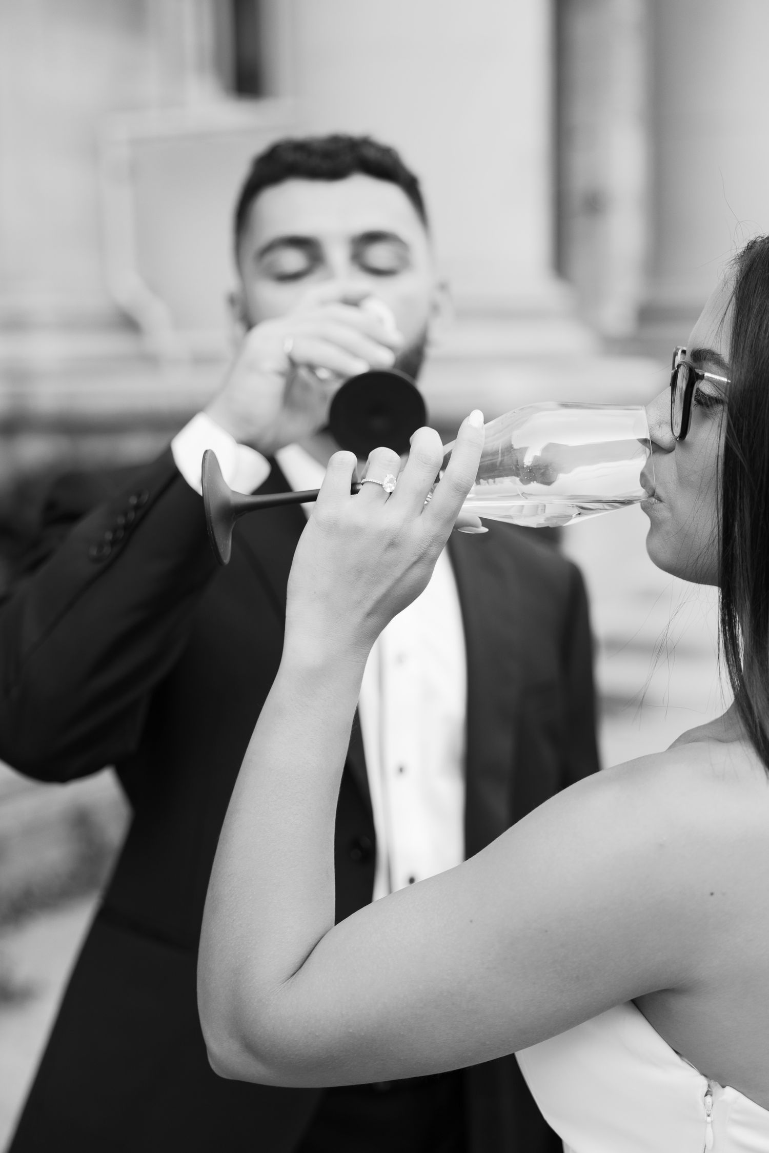 Close-up black and white photo of couple sharing champagne outdoors.