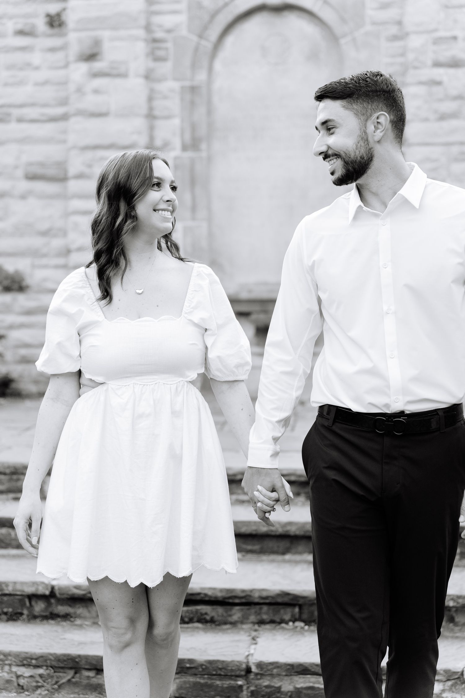 A couple shares a loving glance while walking hand-in-hand on stone steps.