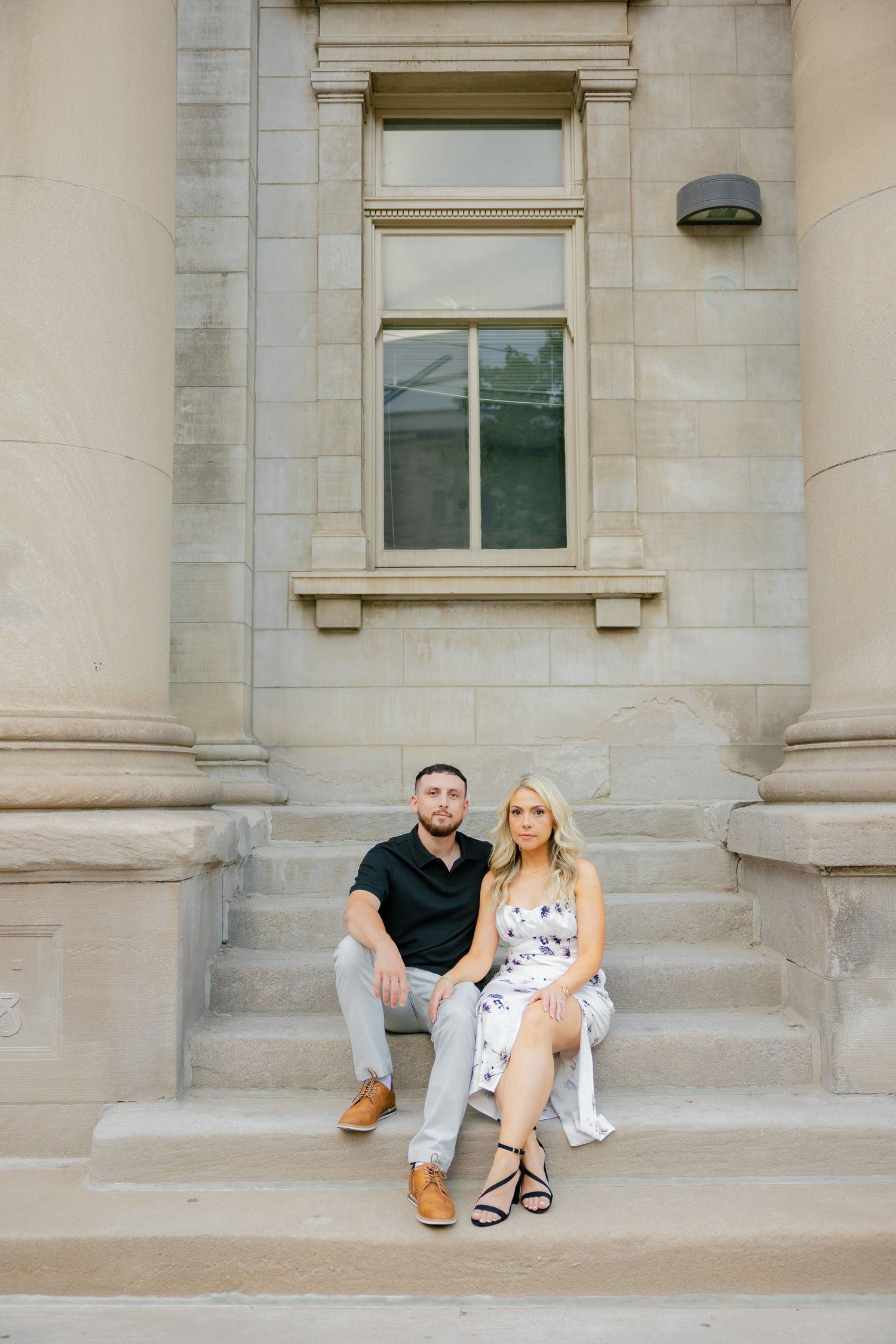 Two people sit together on stone steps between large columns of a classical building.