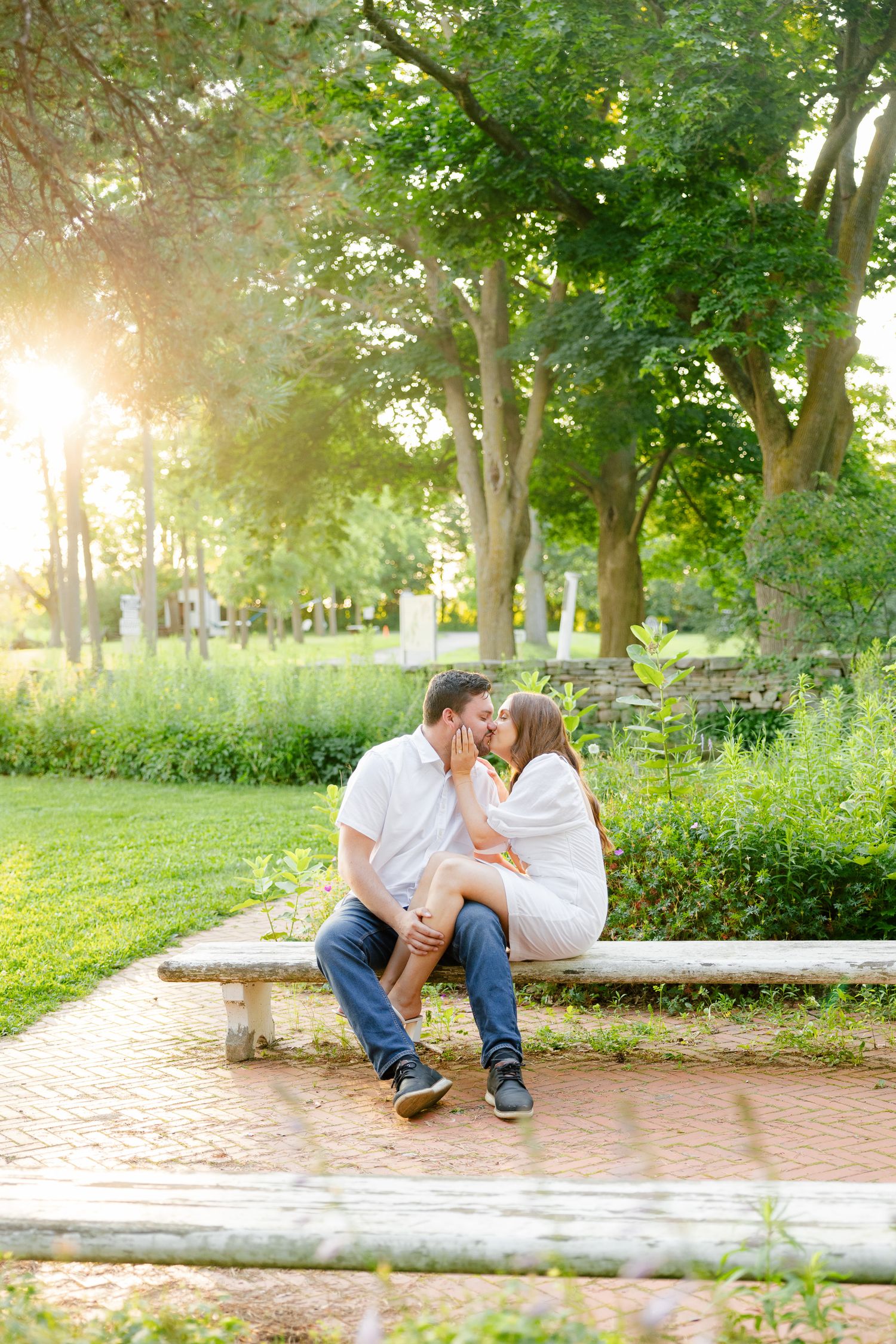 A romantic sunset moment between a couple on a stone bench in a lush garden setting.