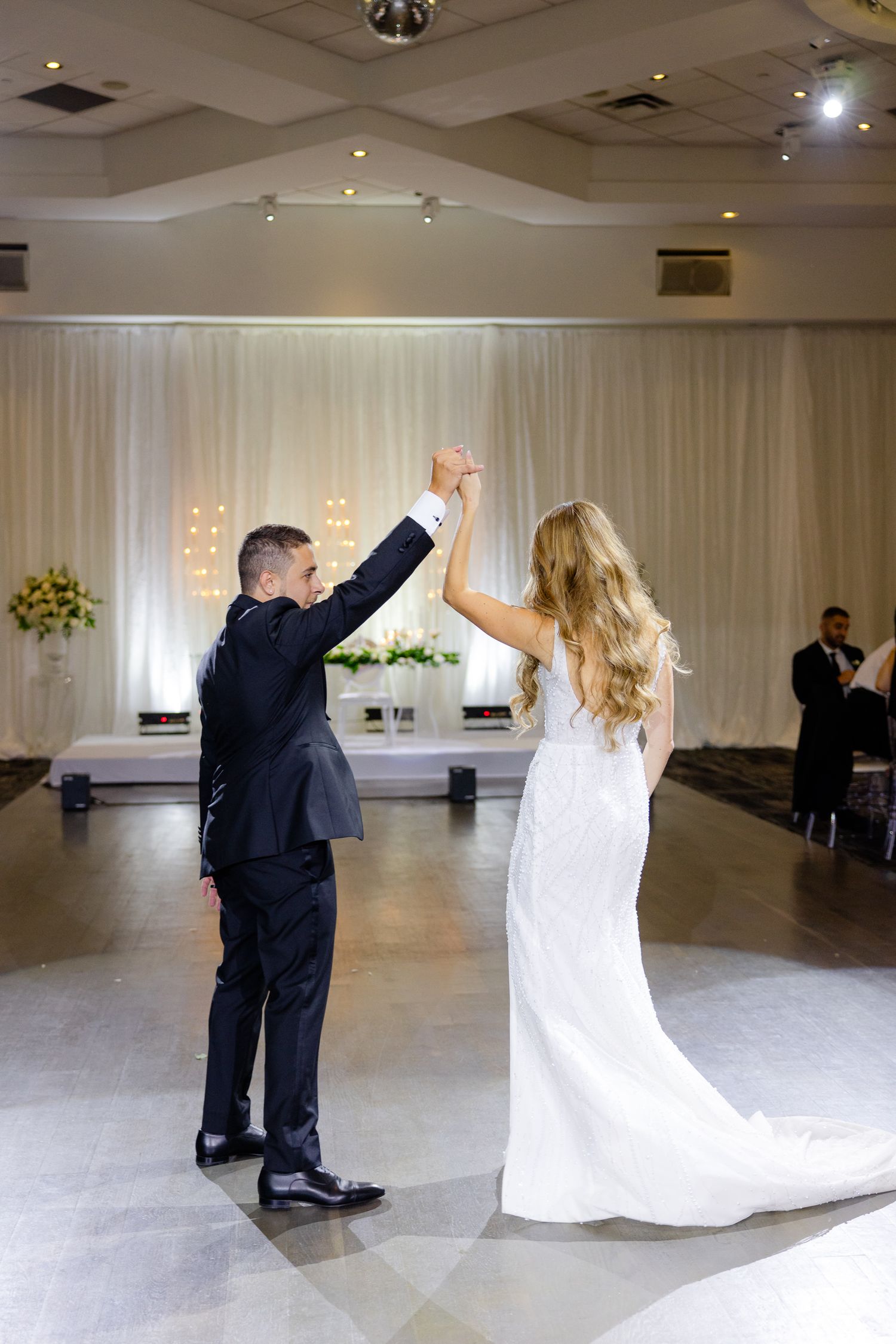 Couple performs celebratory dance moves in elegant white-draped reception venue.