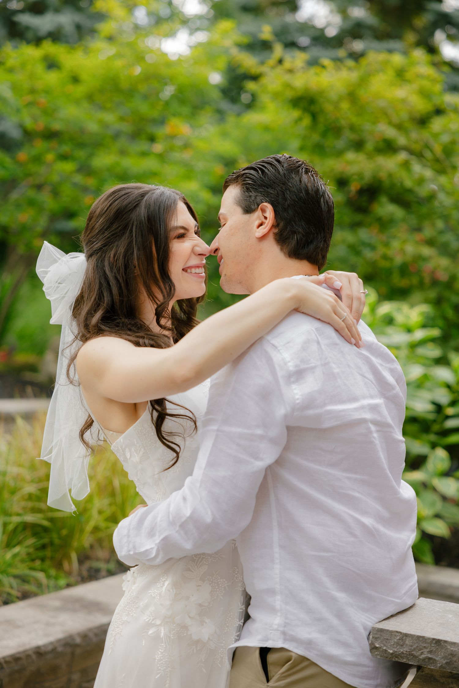 Wedding couple sharing an intimate moment while sitting on stone bench in a lush garden.