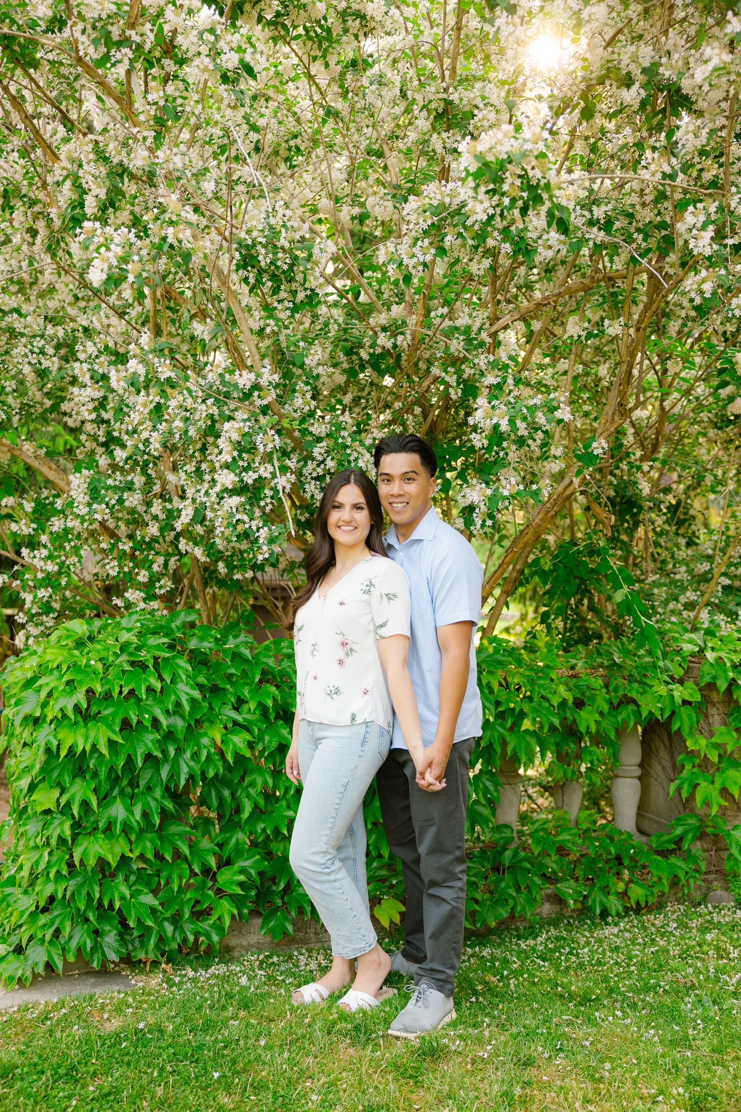 A couple poses together under blooming spring trees during an outdoor photoshoot.