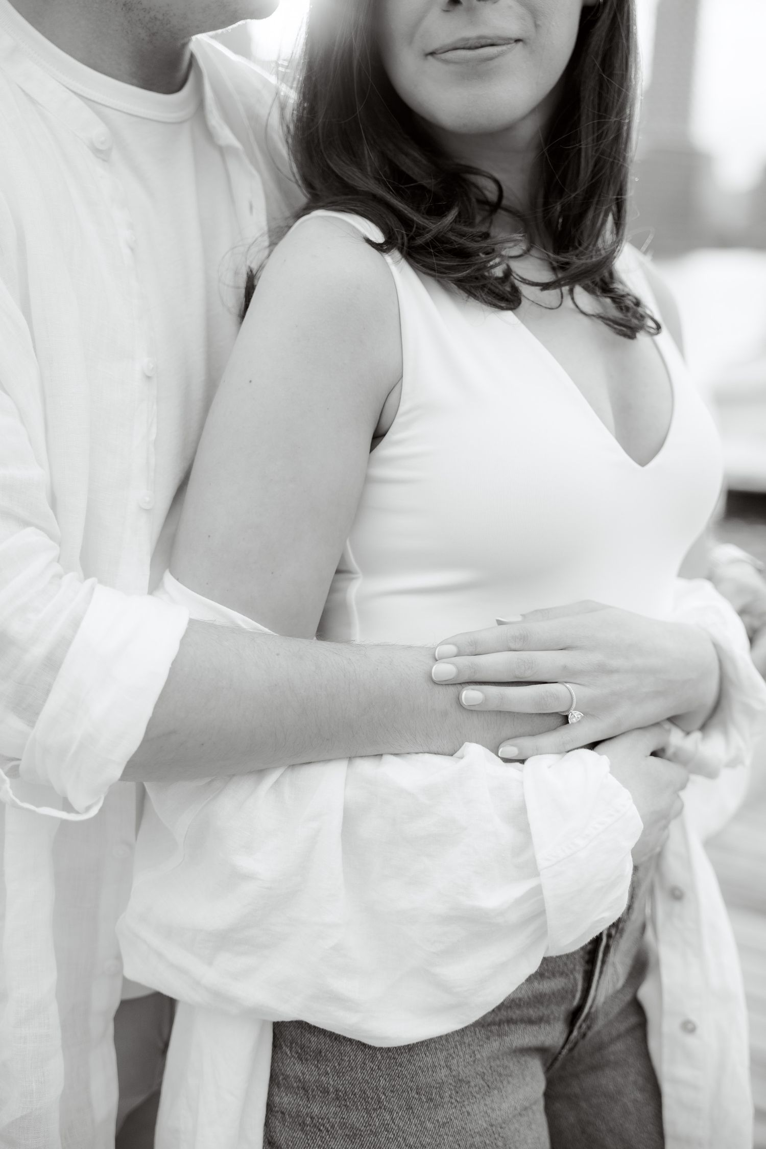 A romantic black and white close-up of a couple embracing, with focus on their white clothing and tender touch.