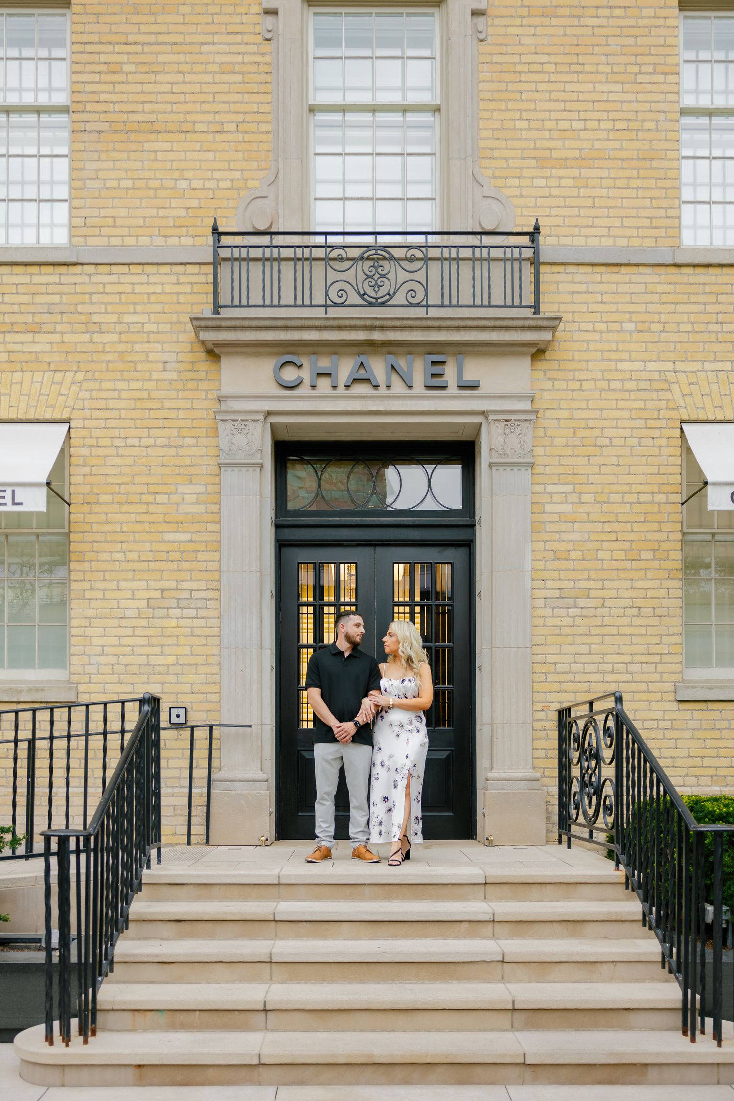 Stylish couple standing in the doorway of a Chanel boutique with elegant architectural details.