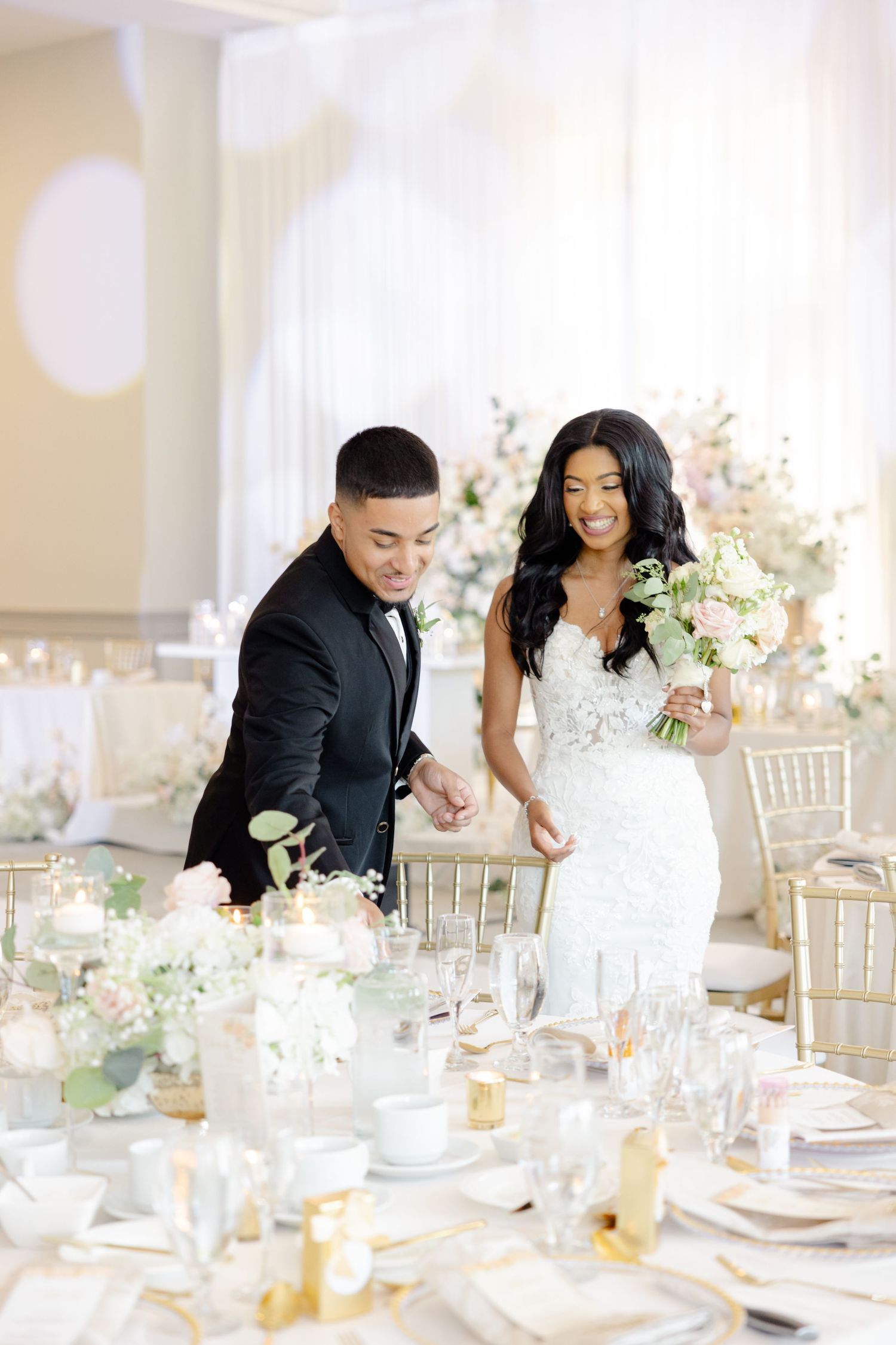 Wedding couple looking at their elegantly decorated reception table with white and gold details.