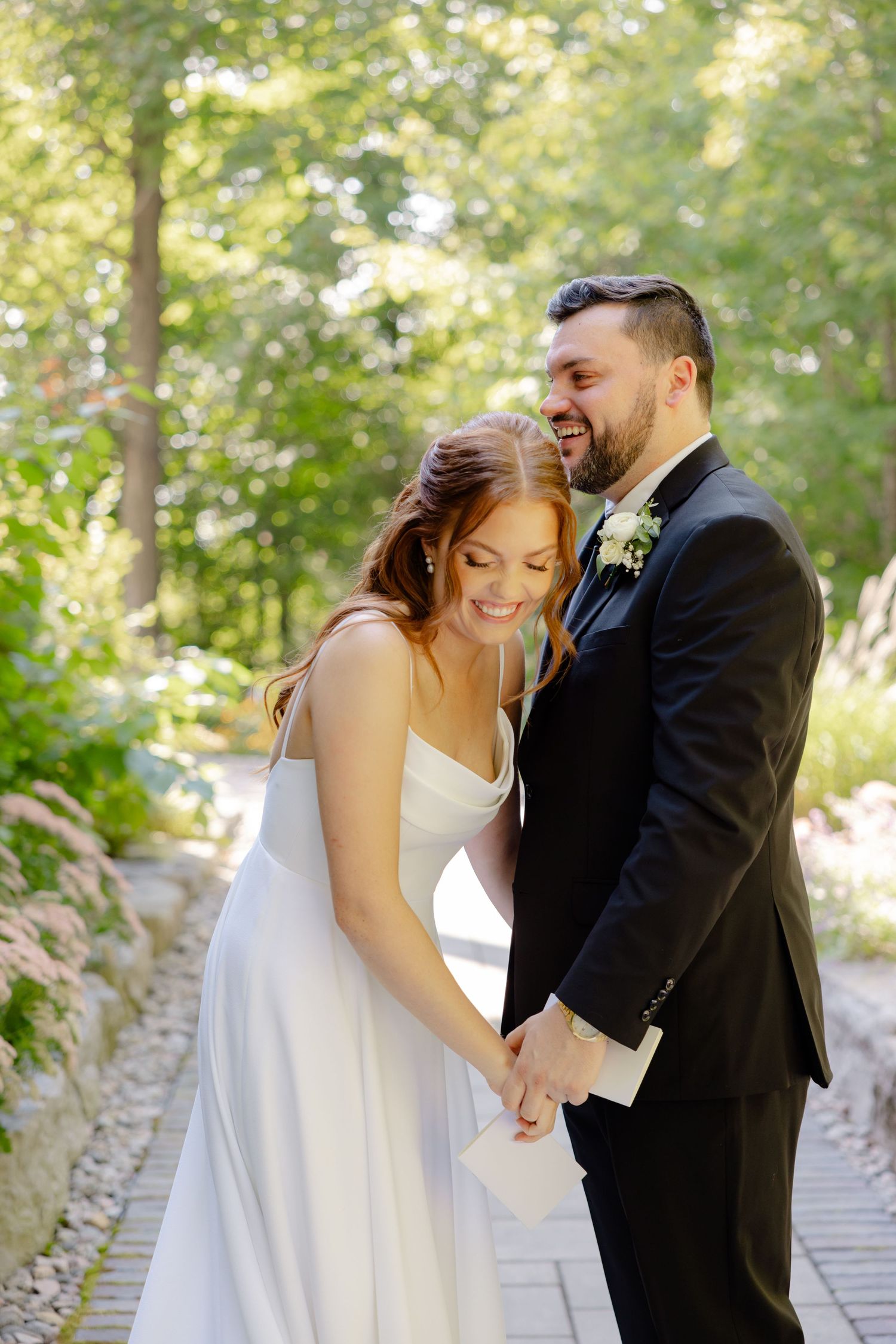 A joyful wedding moment captured on a garden path with natural sunlit foliage in the background.
