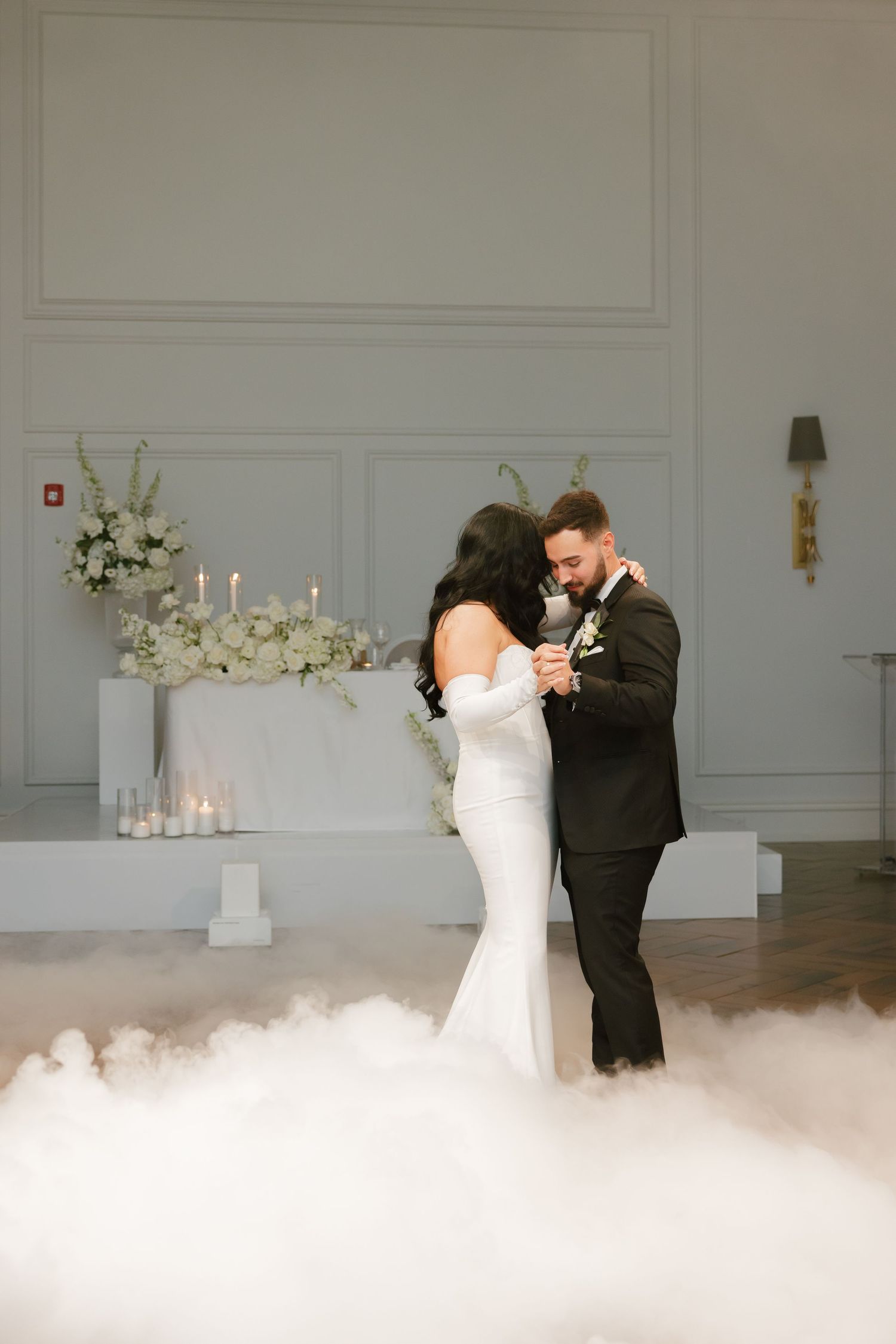 Romantic first dance moment with fog effects and white floral decorations.