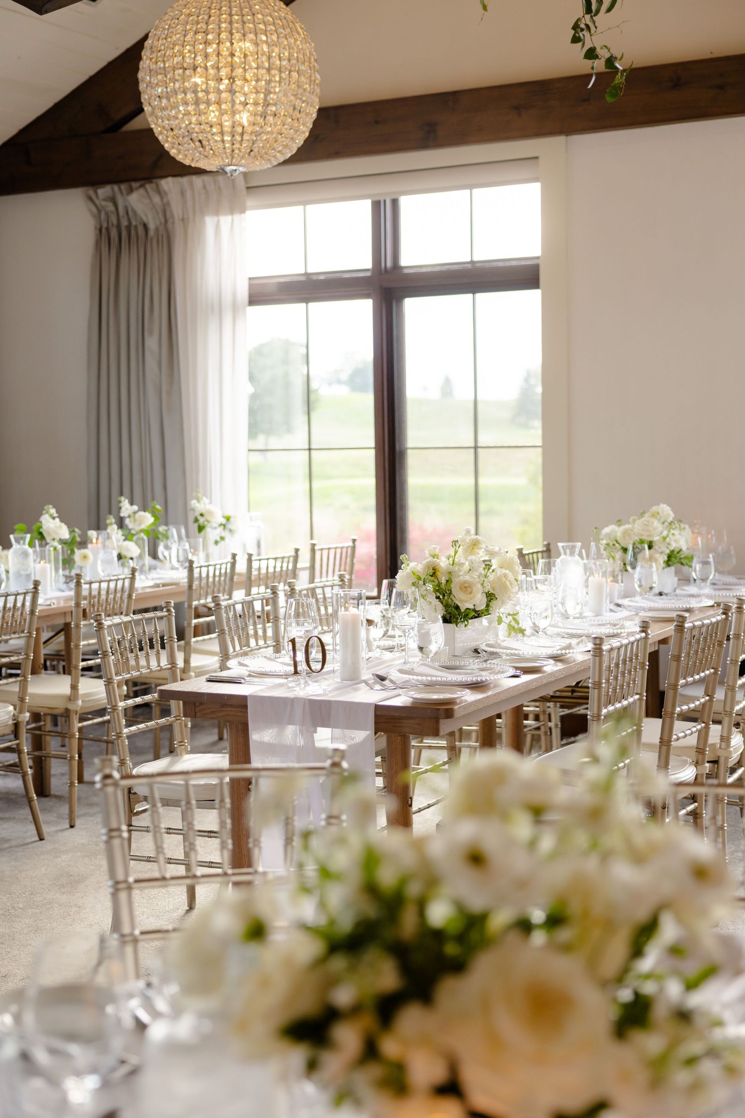 Elegant reception hall with crystal chandelier and gold chiavari chairs set for wedding dinner.