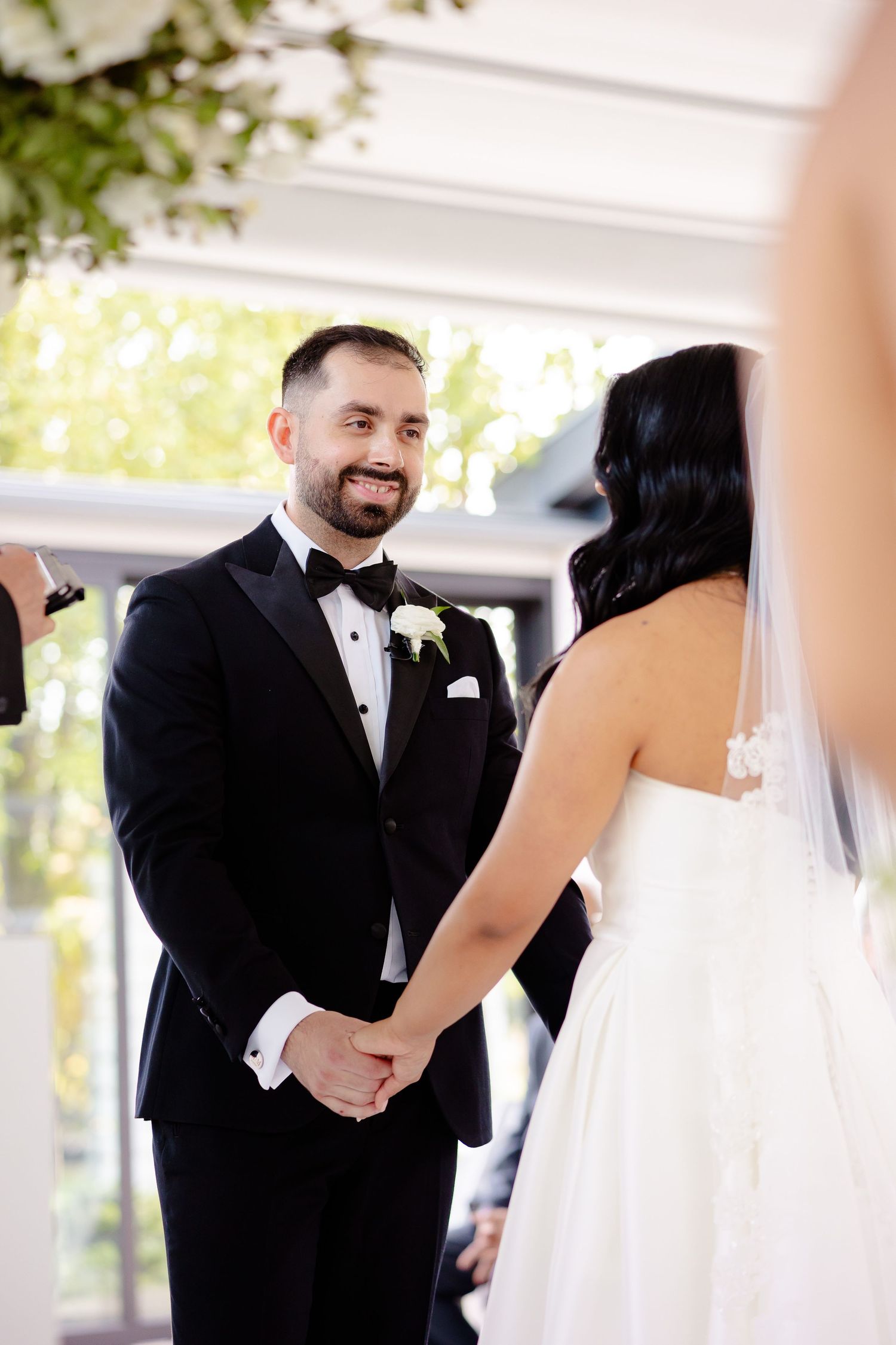 Elegant wedding ceremony moment with couple holding hands during their vows in a bright indoor space.