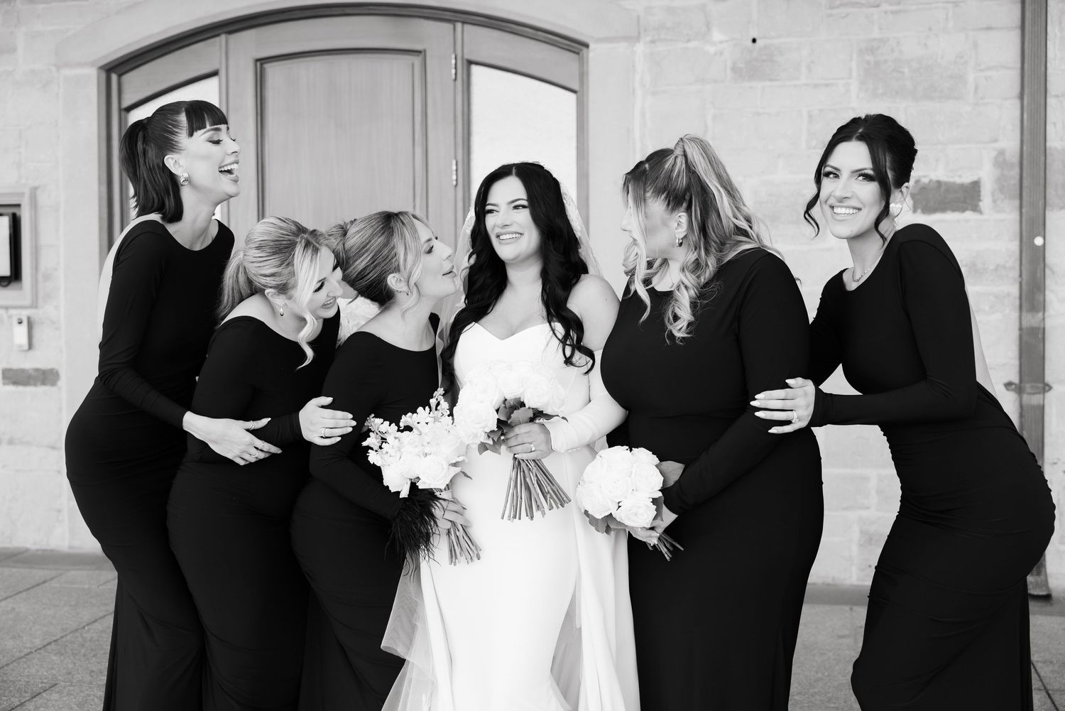 Black and white photo of bridal party laughing together during wedding portraits.