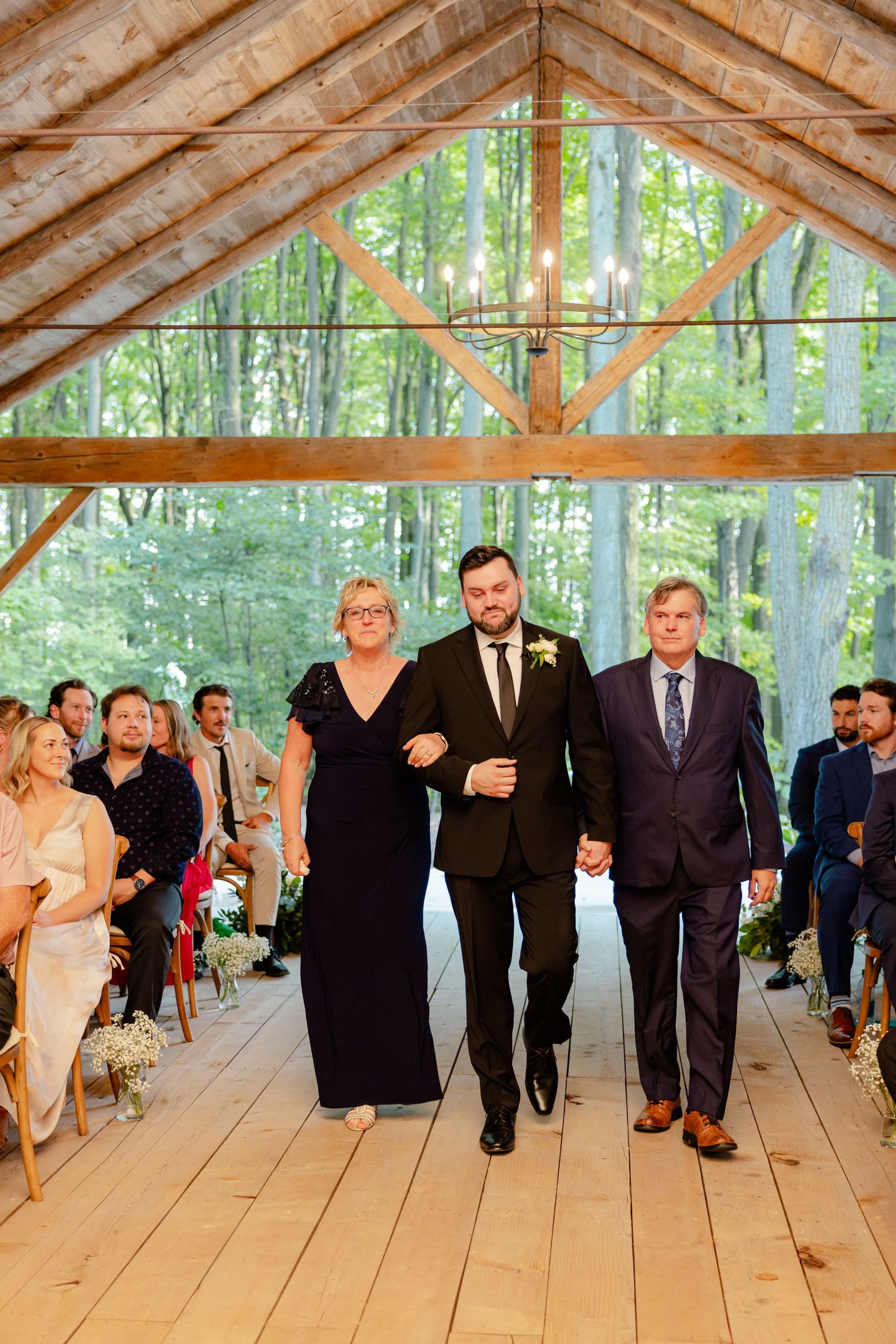 Wedding ceremony processional in a rustic wooden pavilion with exposed beams and forest backdrop.
