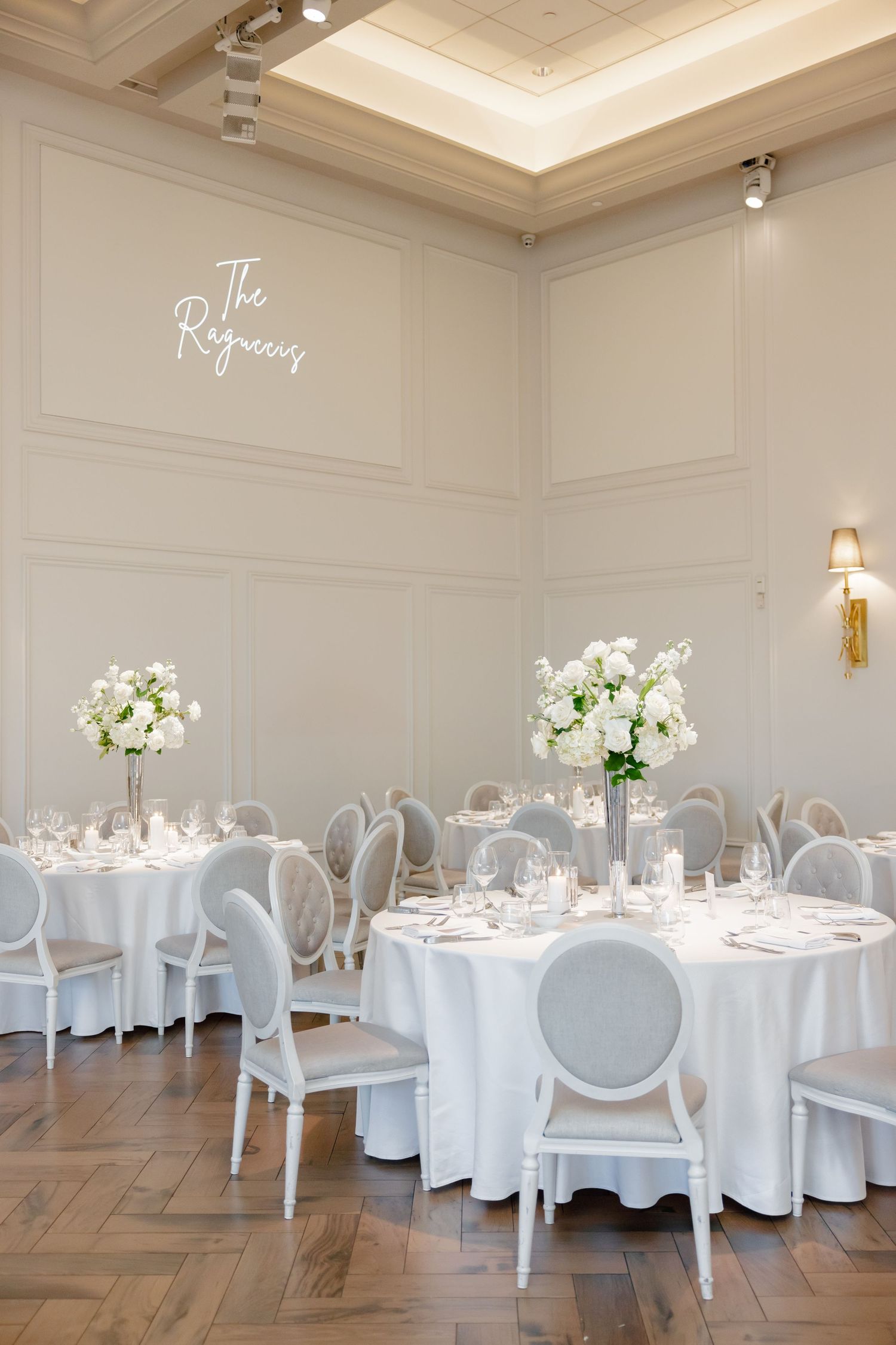 Bright white reception venue with round tables, Louis XVI chairs and floral centerpieces.