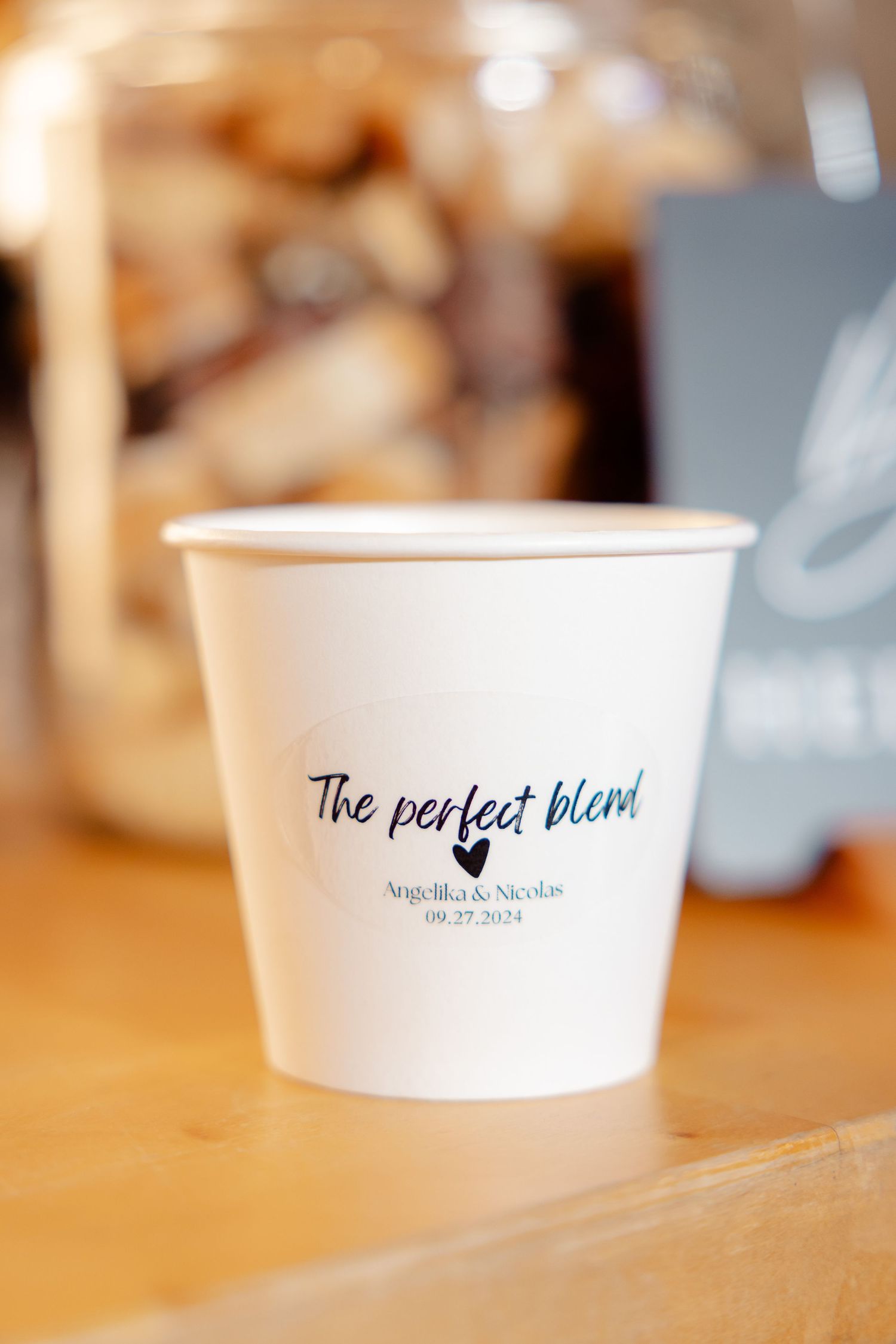 A white disposable coffee cup with 'The perfect blend' text and a wedding date printed on it.