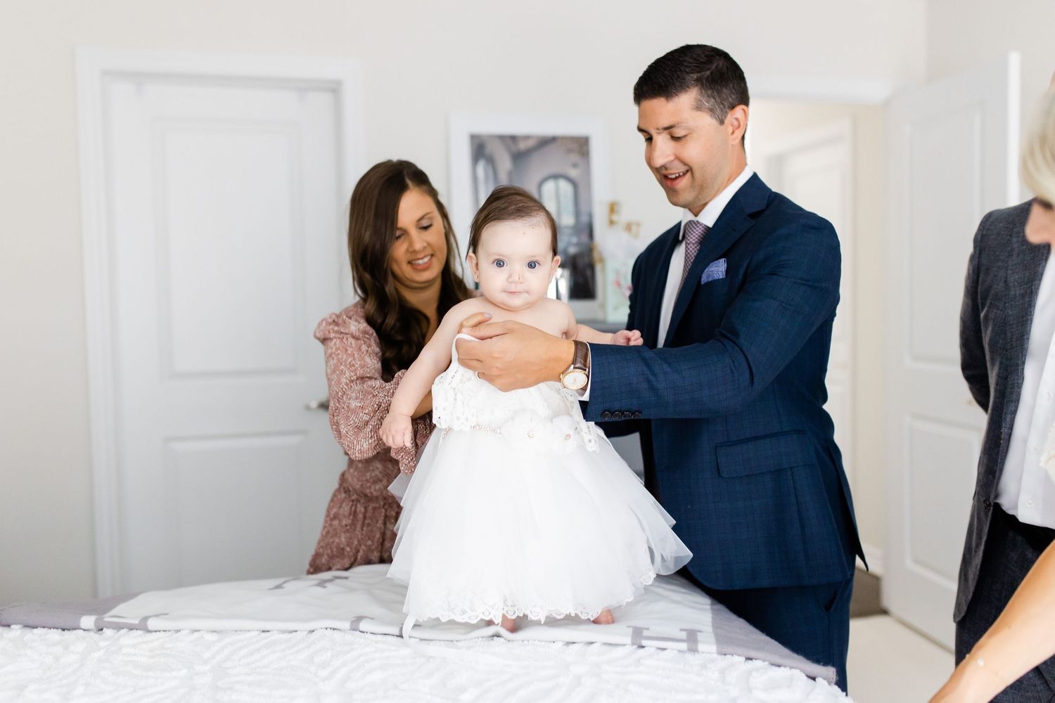A group in formal wear gathers around a small child in a white dress.